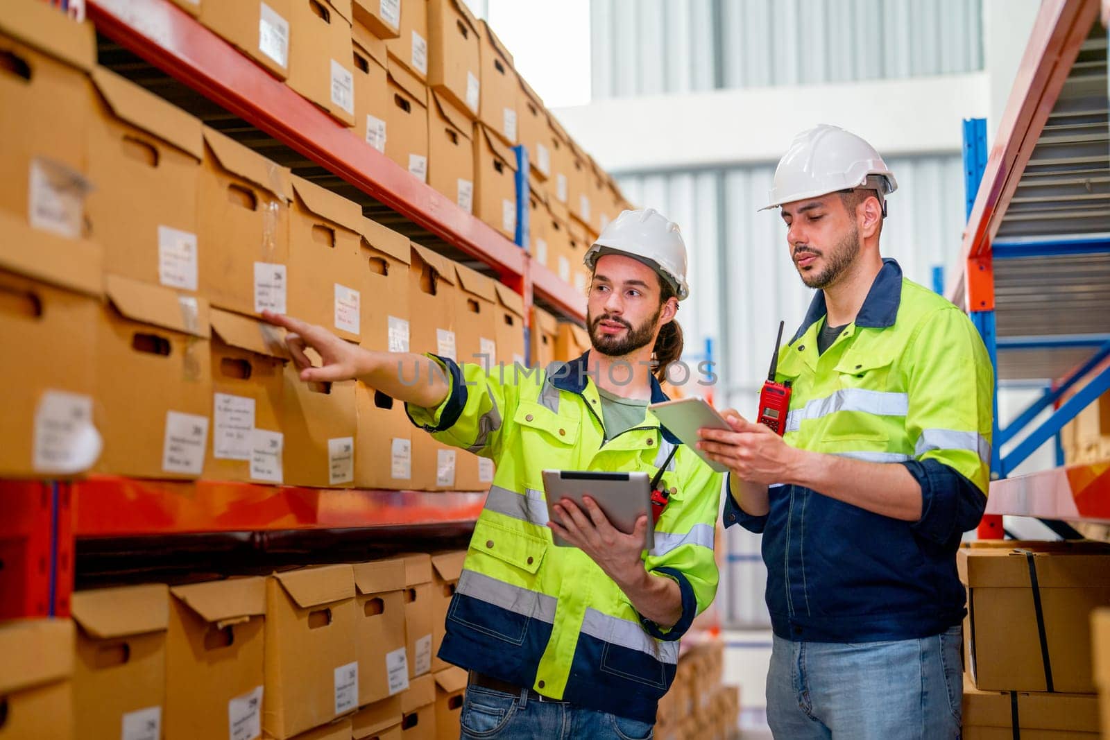 Two professional warehouse workers stand between shelves of products with one point to the box and discuss together about work in workplace area. by nrradmin