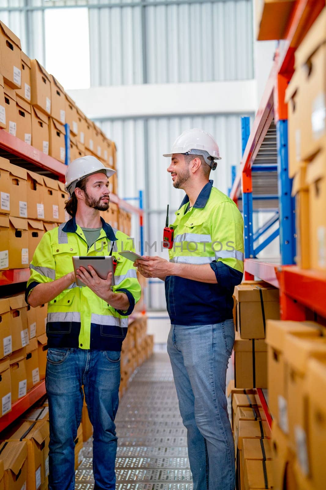 Two professional warehouse workers stand between shelves of products and discuss together about work in workplace area. The concept of good system support the worker for stock and shipment industry.