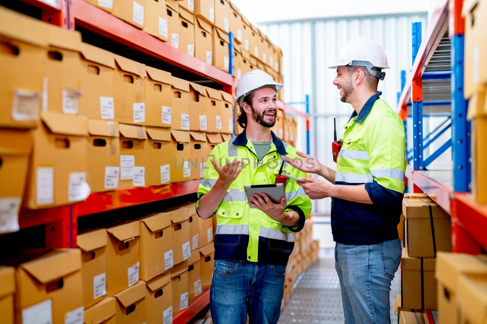 Two professional warehouse worker men discuss about work and stay between shelves with product in workplace and they look happy. by nrradmin
