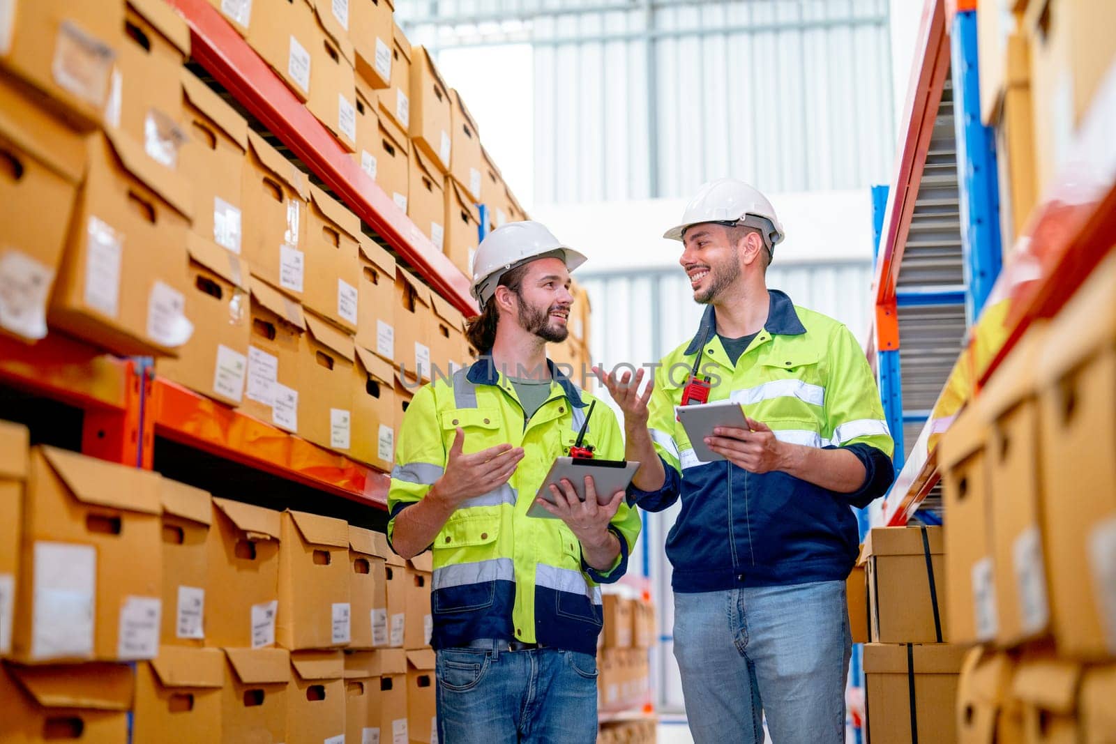 Two professional warehouse worker men hold tablet and discuss about work together also stay between shelves with product in workplace and they look happy. by nrradmin