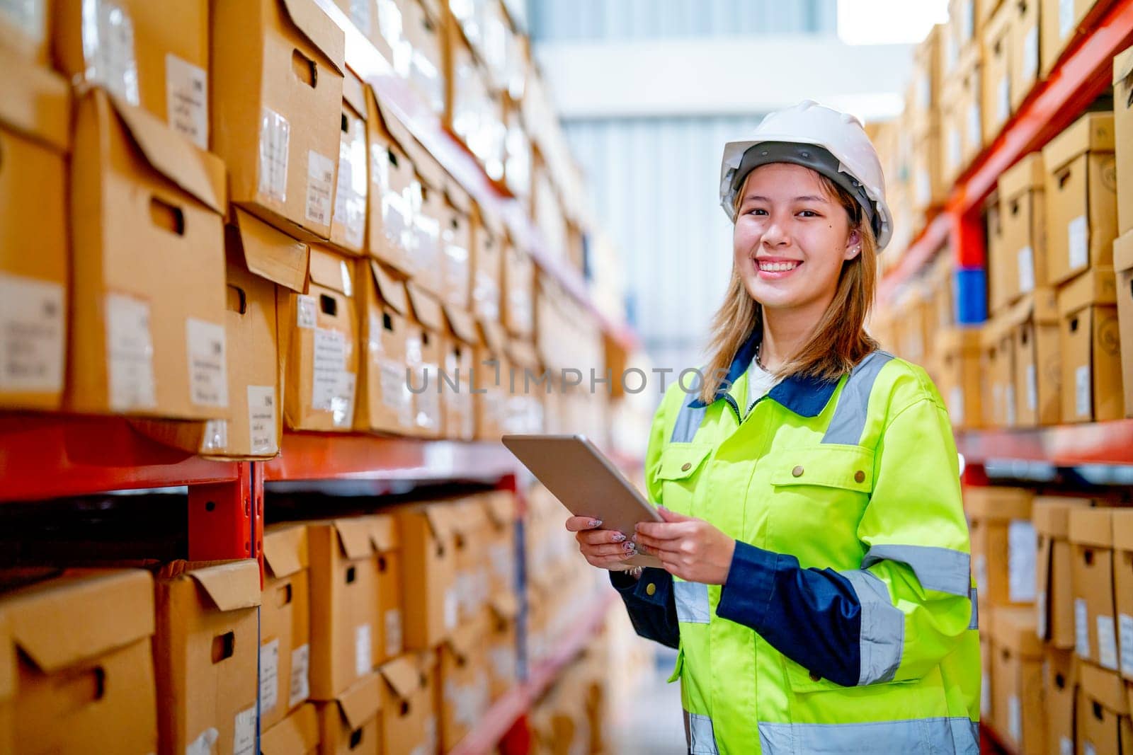 Portrait of young warehouse worker woman hold tablet and look at camera also stand between shelves