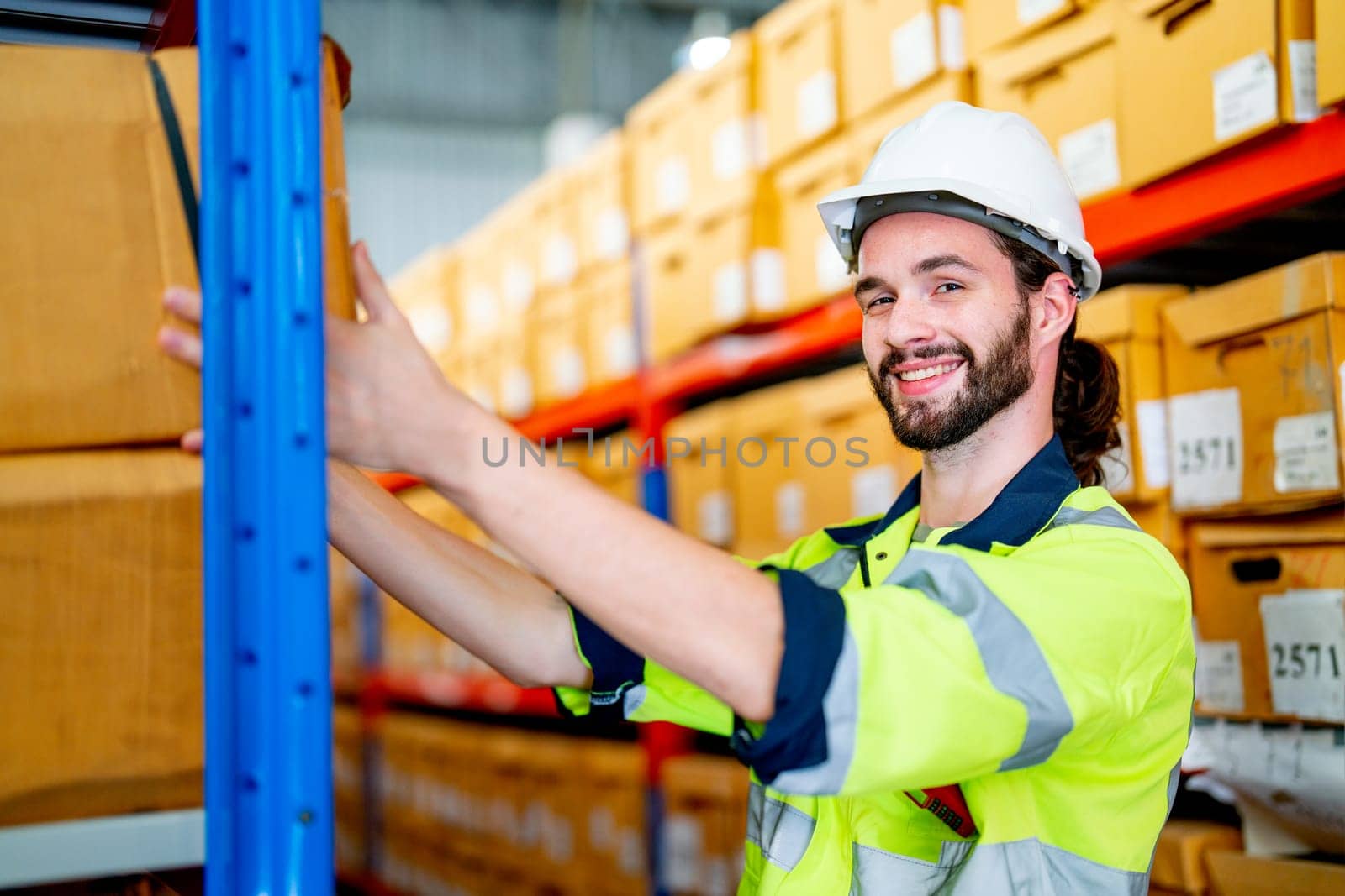 Close up smart warehouse worker man hold box on shelves also look at camera with smiling stay in workplace area. by nrradmin