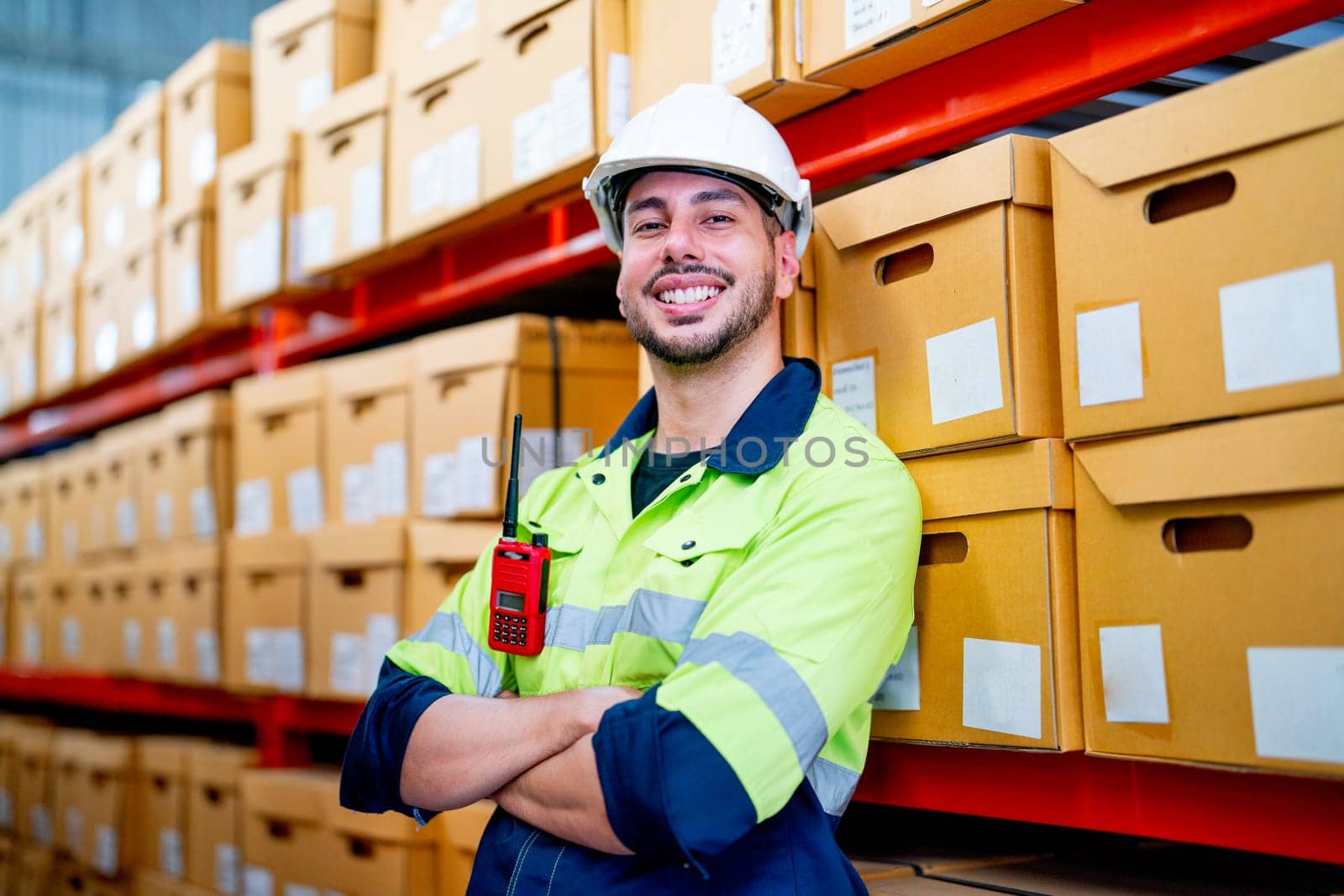 Smart warehouse worker stand and lean against the product boxes on shelves and also look at camea with smiling in workplace.