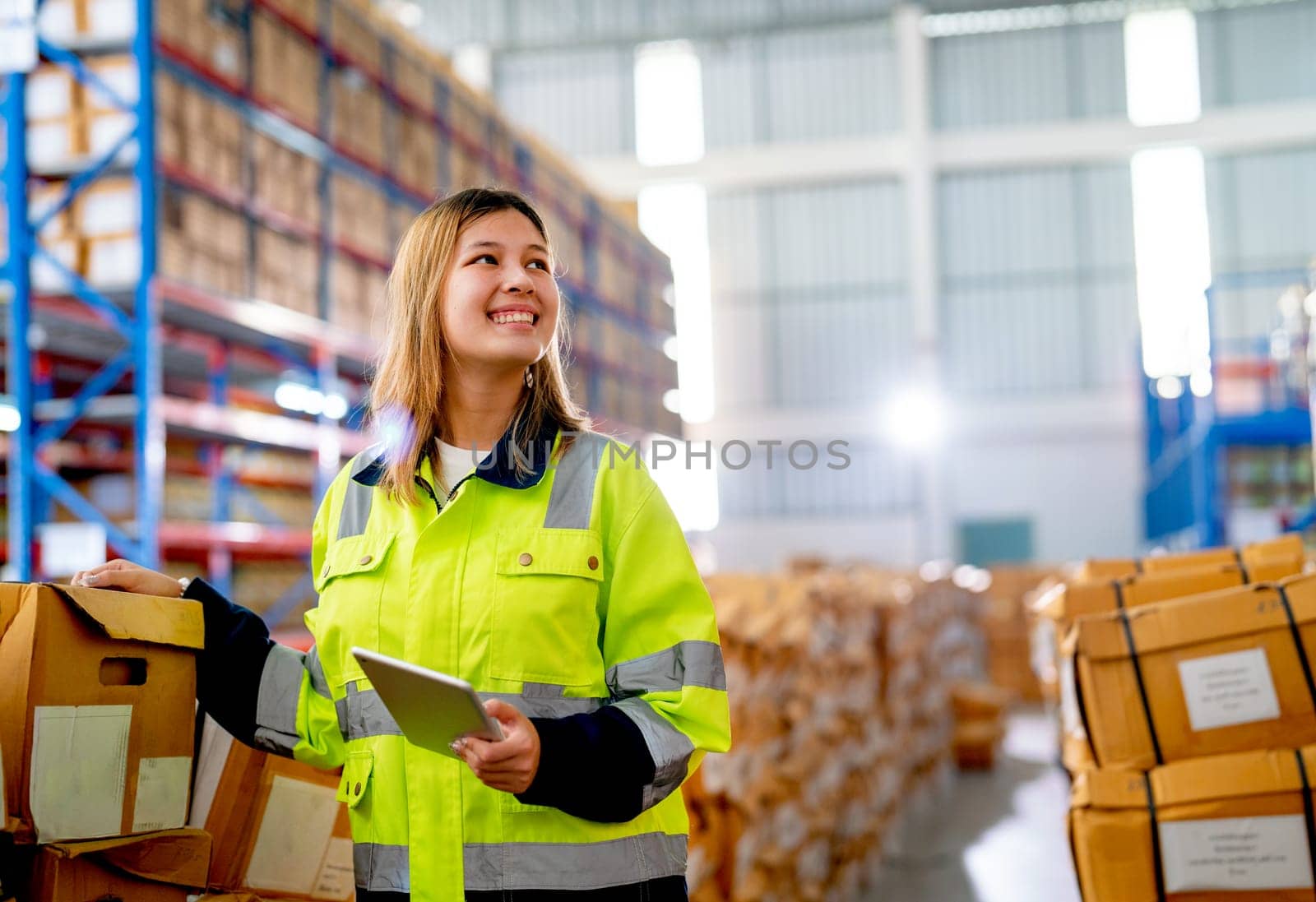 Beautiful young warehouse worker woman hold tablet and smiling also look to her left side in workplace area. by nrradmin