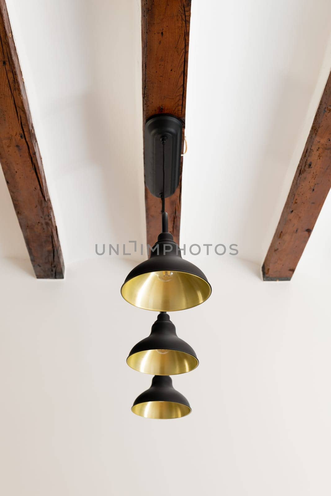 Metal chandelier with light-bulbs fastened to old wooden ceiling beam. Home light equipment in interior design. Vintage element of decor