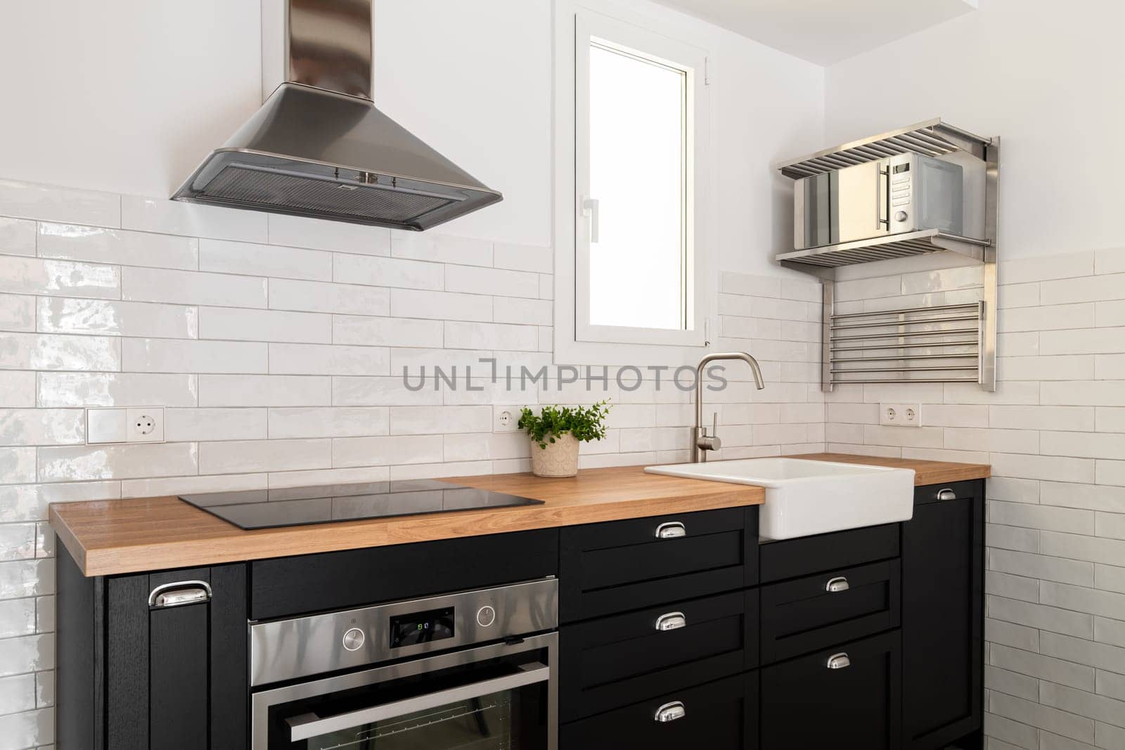 Comfortable and stylish kitchen in Scandinavian minimalist style with wooden countertops and black fronts on the background of white tiles. Kitchen concept in modern European residential complexes by apavlin