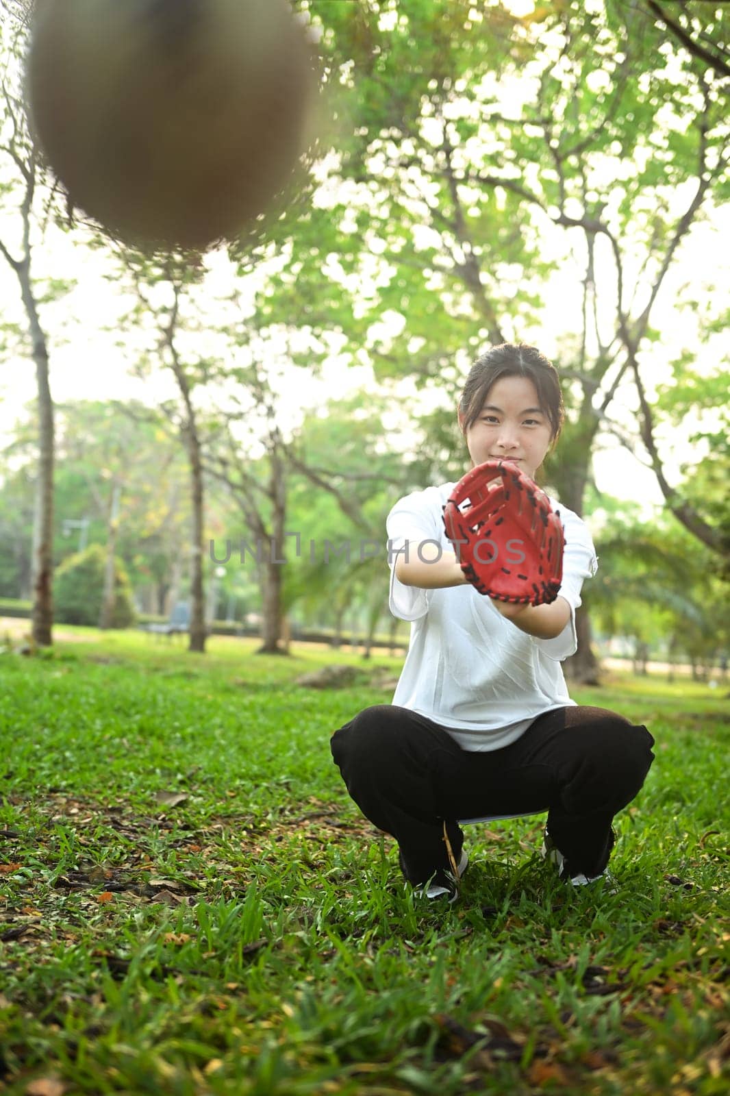 Shot of teenaged Asian girl catching a baseball in the park. Sports and youth lifestyle concept by prathanchorruangsak