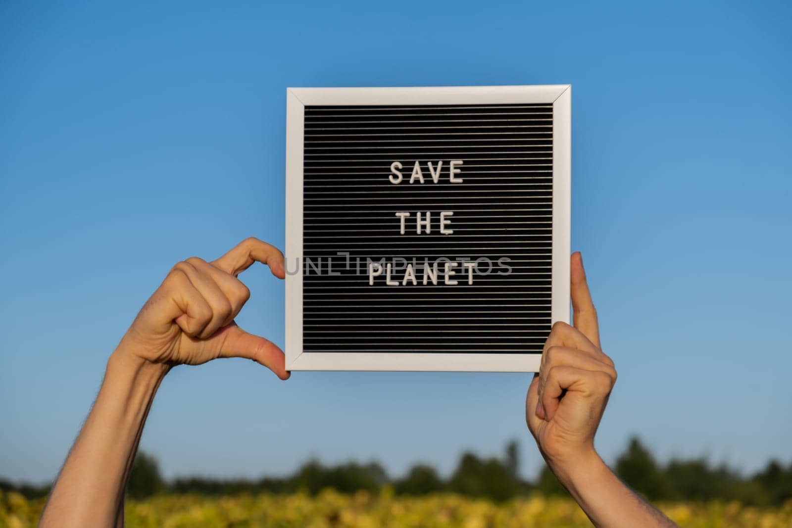 Hands of protester in shape of heart with text SAVE THE PLANET on black board on background of sunflower field. Reuse reduce recycle concept. Protesting for nature Climate strike volunteer protest against earth pollution, global warming