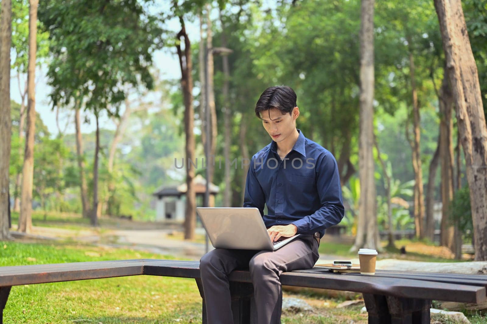 Portrait of young businessman working with laptop in the public park on sunny summer day.