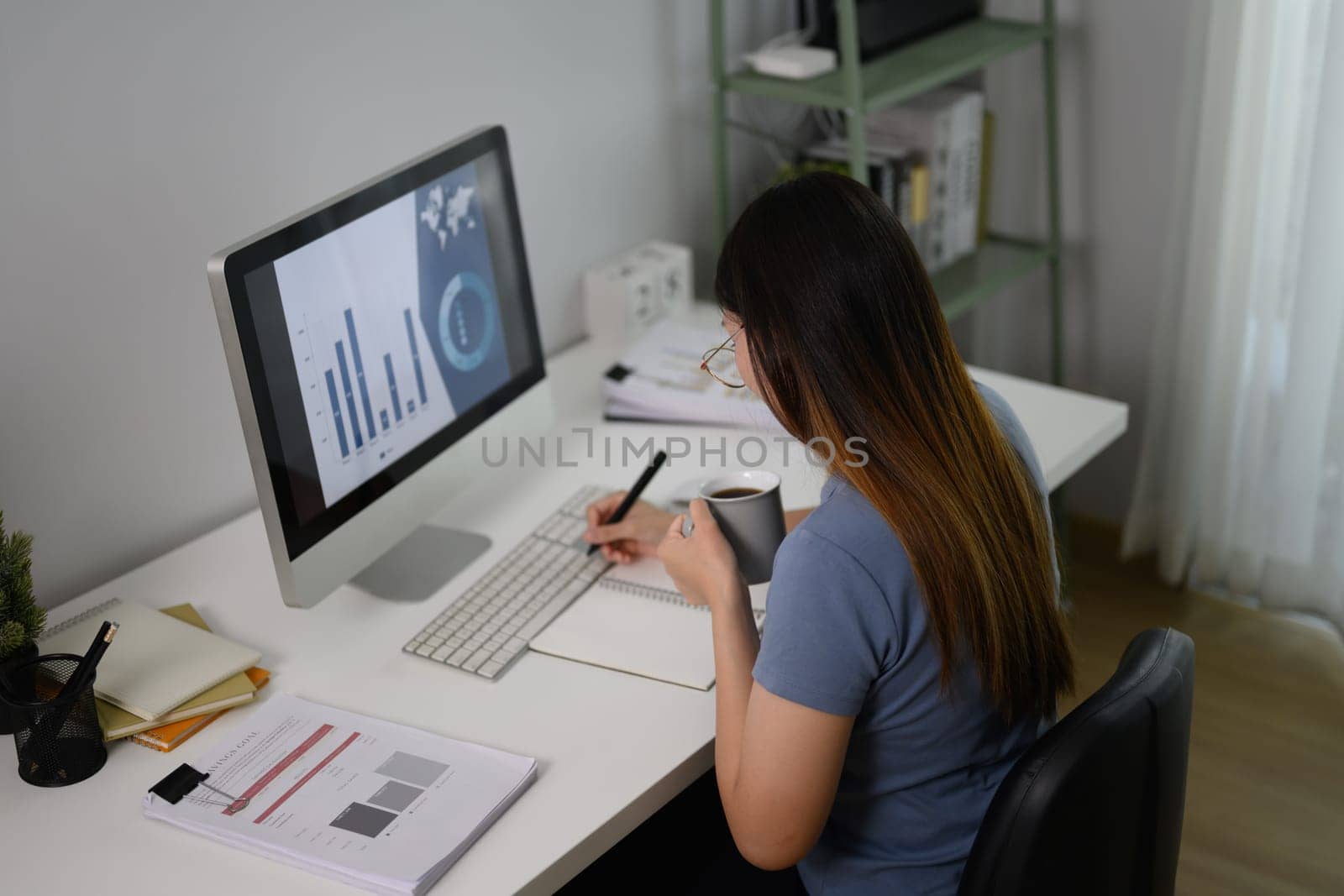 Side view of young businesswoman making notes in note pad sitting at home office.