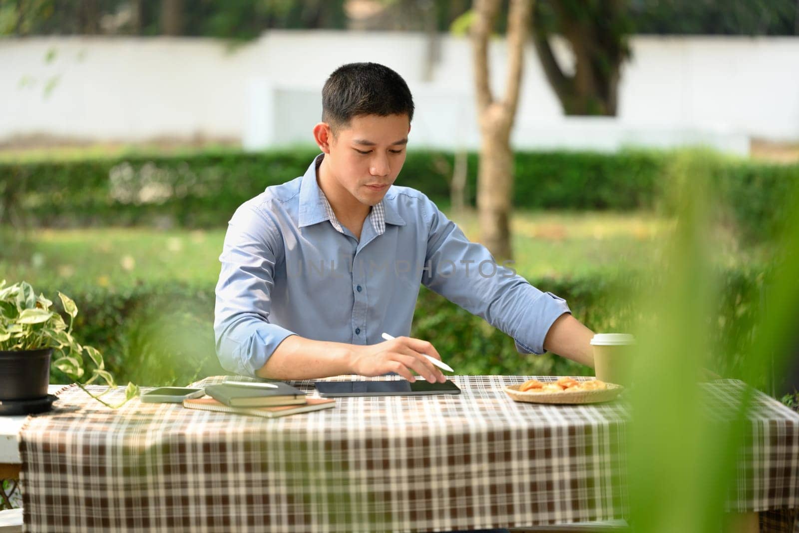 Young businessman working on digital tablet while sitting at table outdoors.