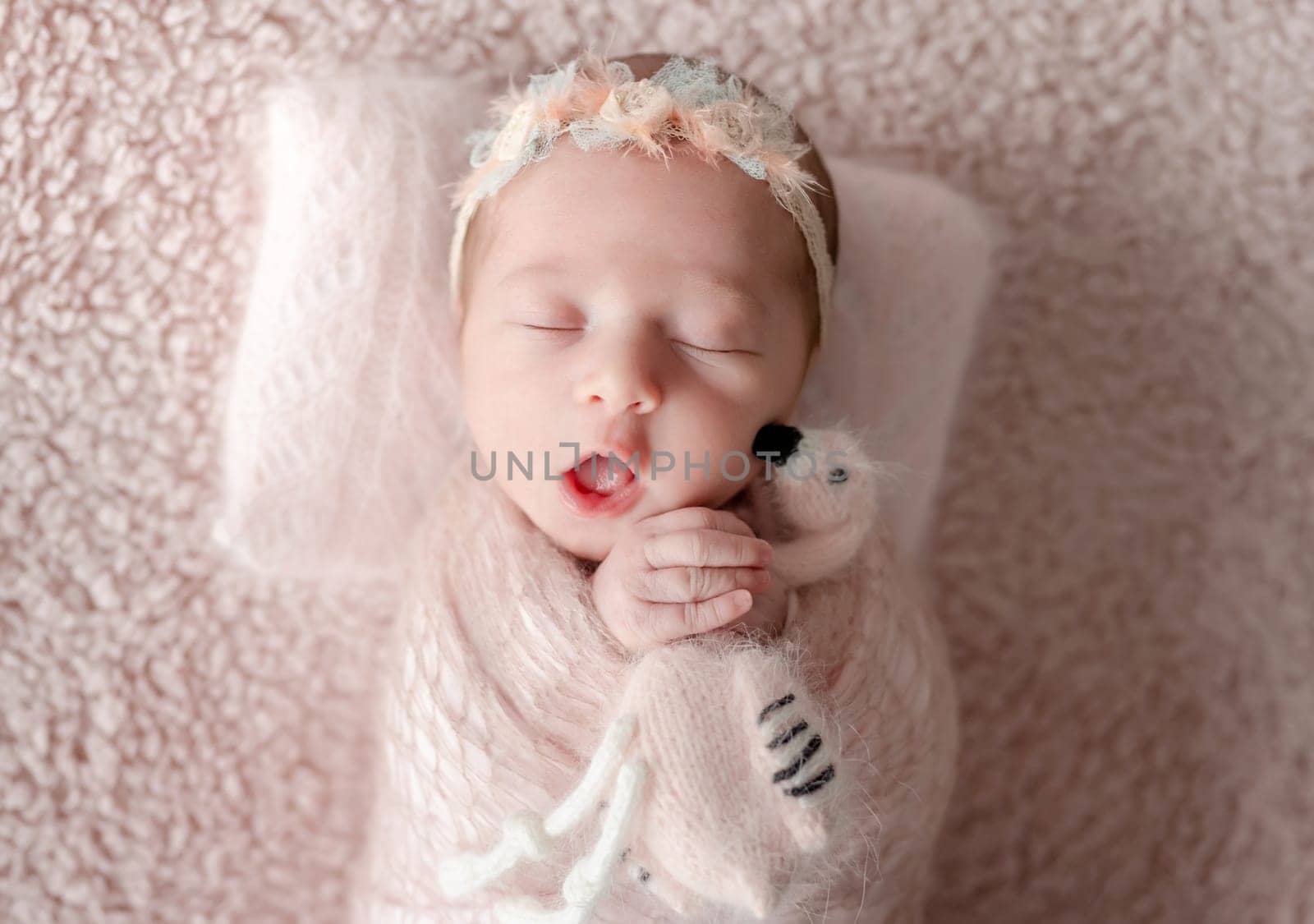Newborn Girl Wrapped In A Blanket With A Flamingo Toy In Her Hands Yawns During A Professional Newborn Photoshoot