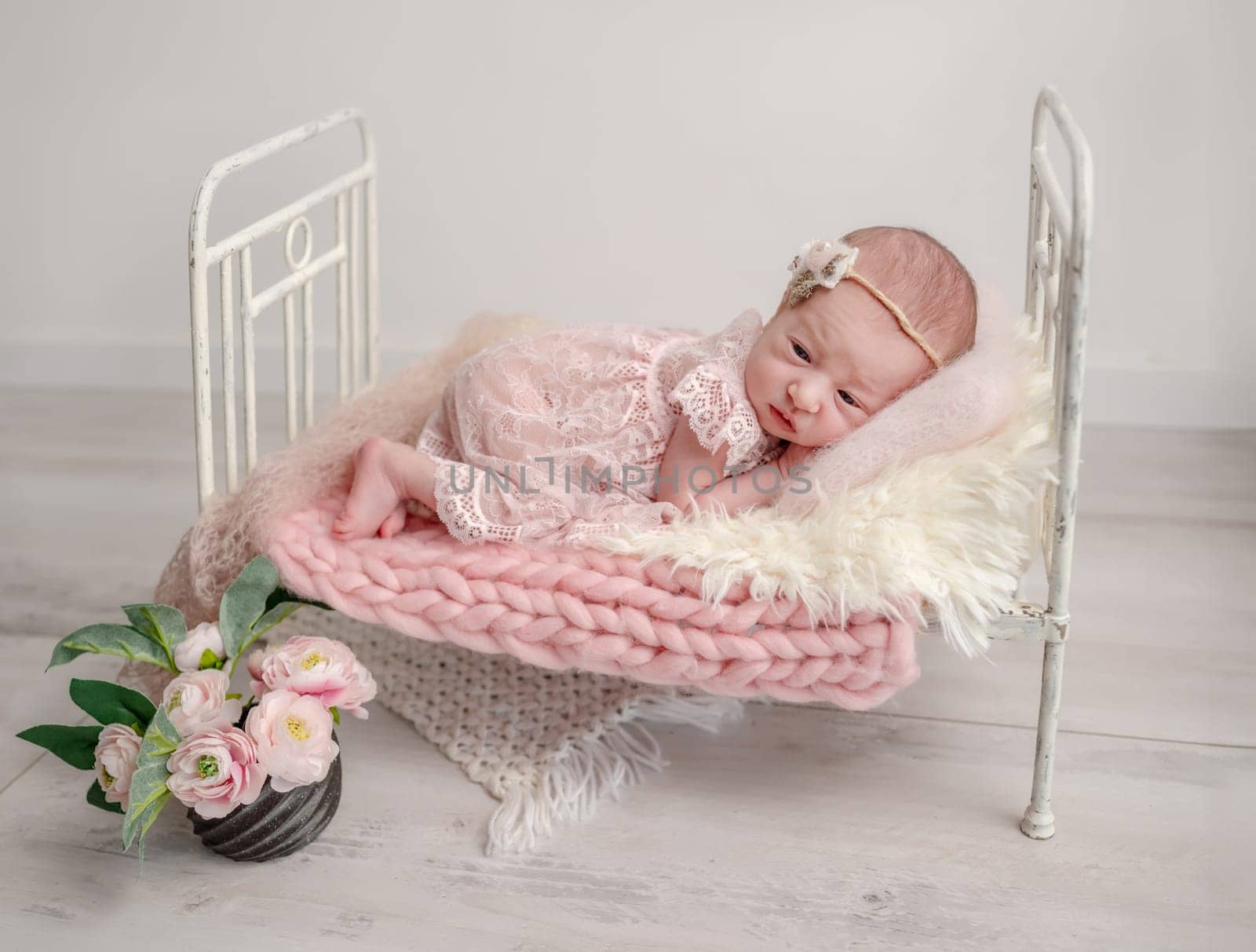 Newborn Girl In Lace Dress Sleeps In Tiny Crib, Captured In Professional Photo With Pink Tones