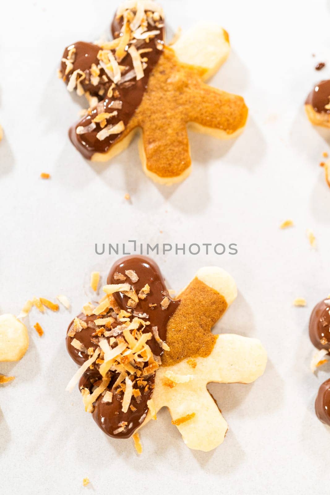 Gingerbread men cookies, chocolate-dipped feet, generously sprinkled with golden toasted coconut shavings, artfully arranged on parchment paper.