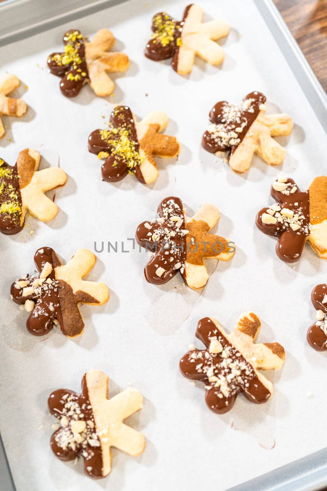 Crafting star-shaped holiday cookies dipped in chocolate and sprinkled with crushed pistachios, arranged on parchment paper.