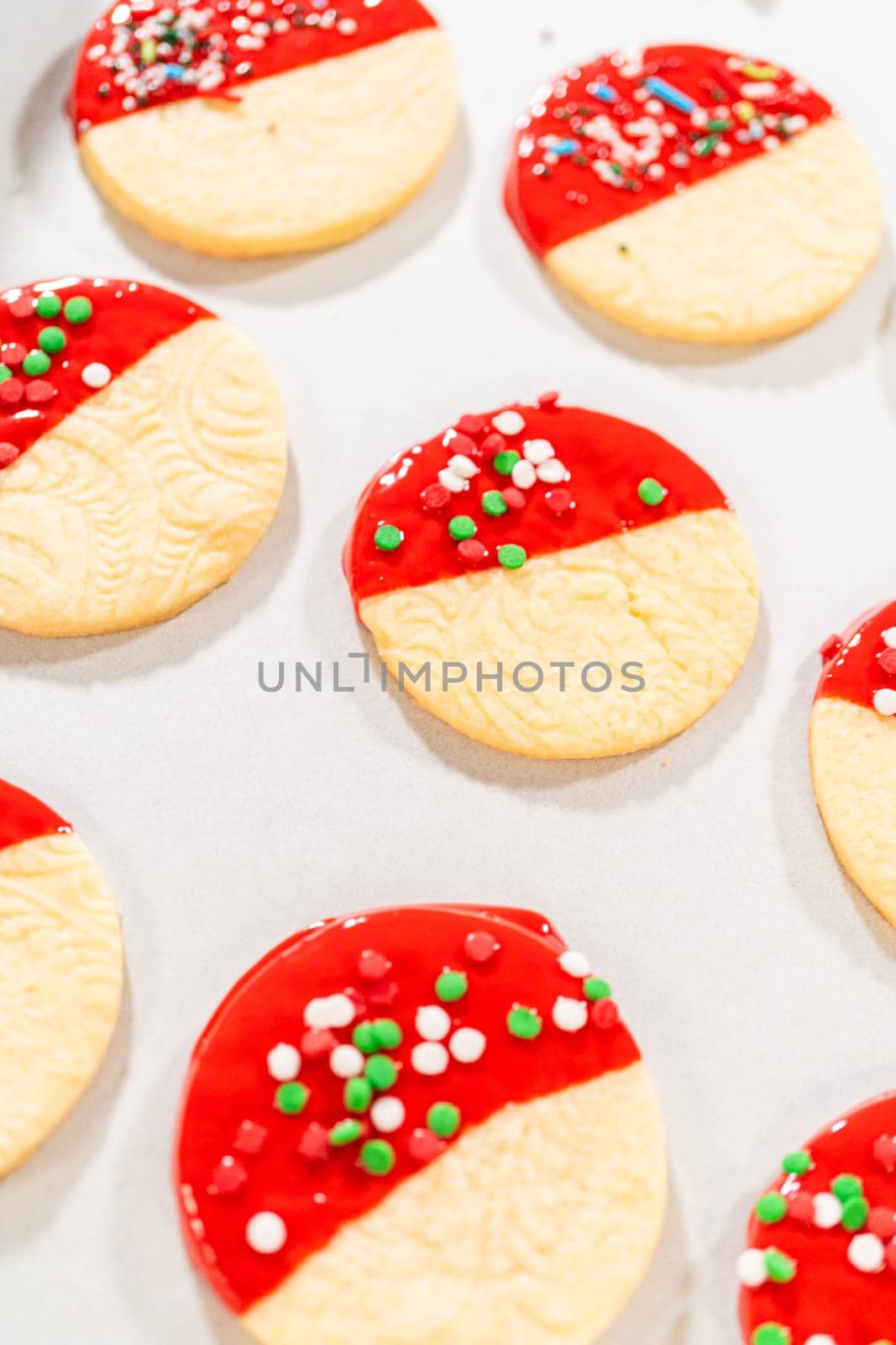 Skillfully decorating cookies with vibrant red melted chocolate and a generous sprinkle of vibrant green, creating a festive holiday treat.