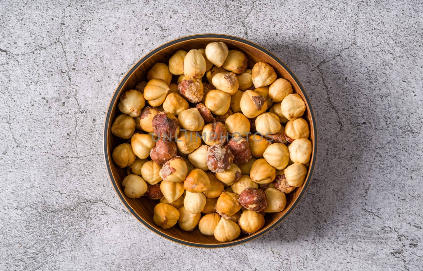 Roasted salted hazelnuts in wooden bowl on stone table by Sonat