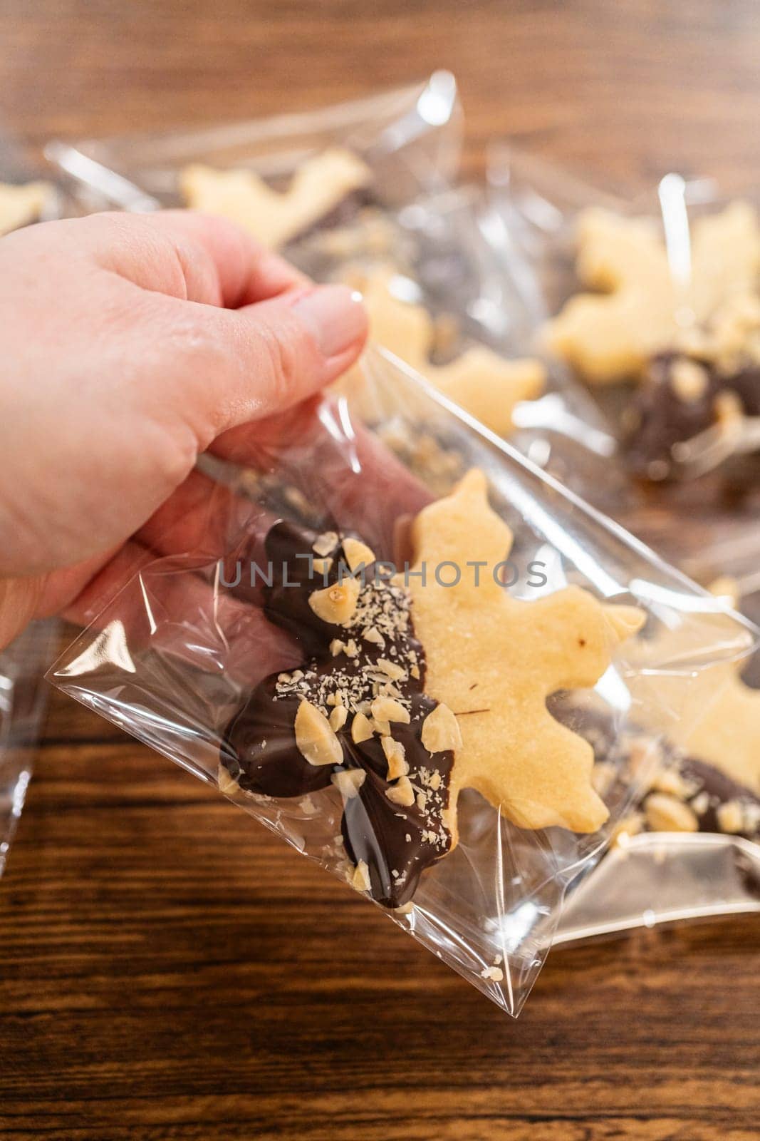 Carefully packaging Christmas cutout cookies, half-dipped in chocolate and presented in clear cellophane wrapping, perfect for festive gifting.