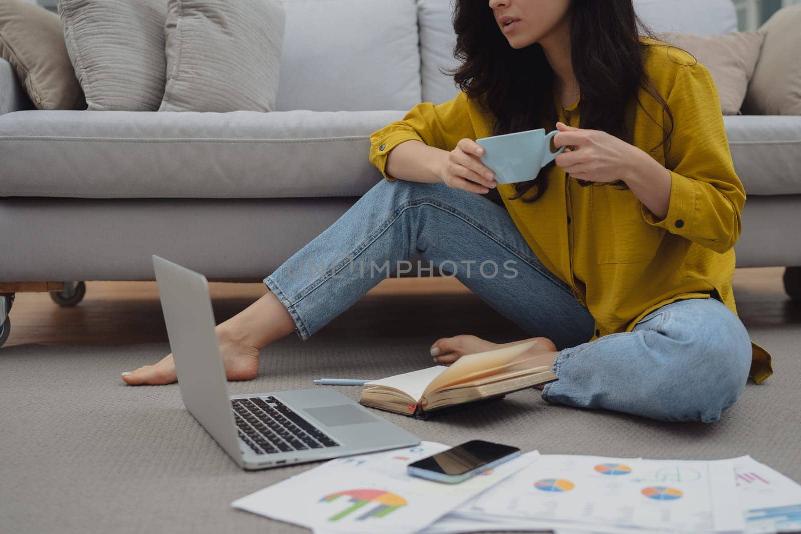 Thoughtful young woman in eyewear using computer while sitting on the sofa at home. High quality photo