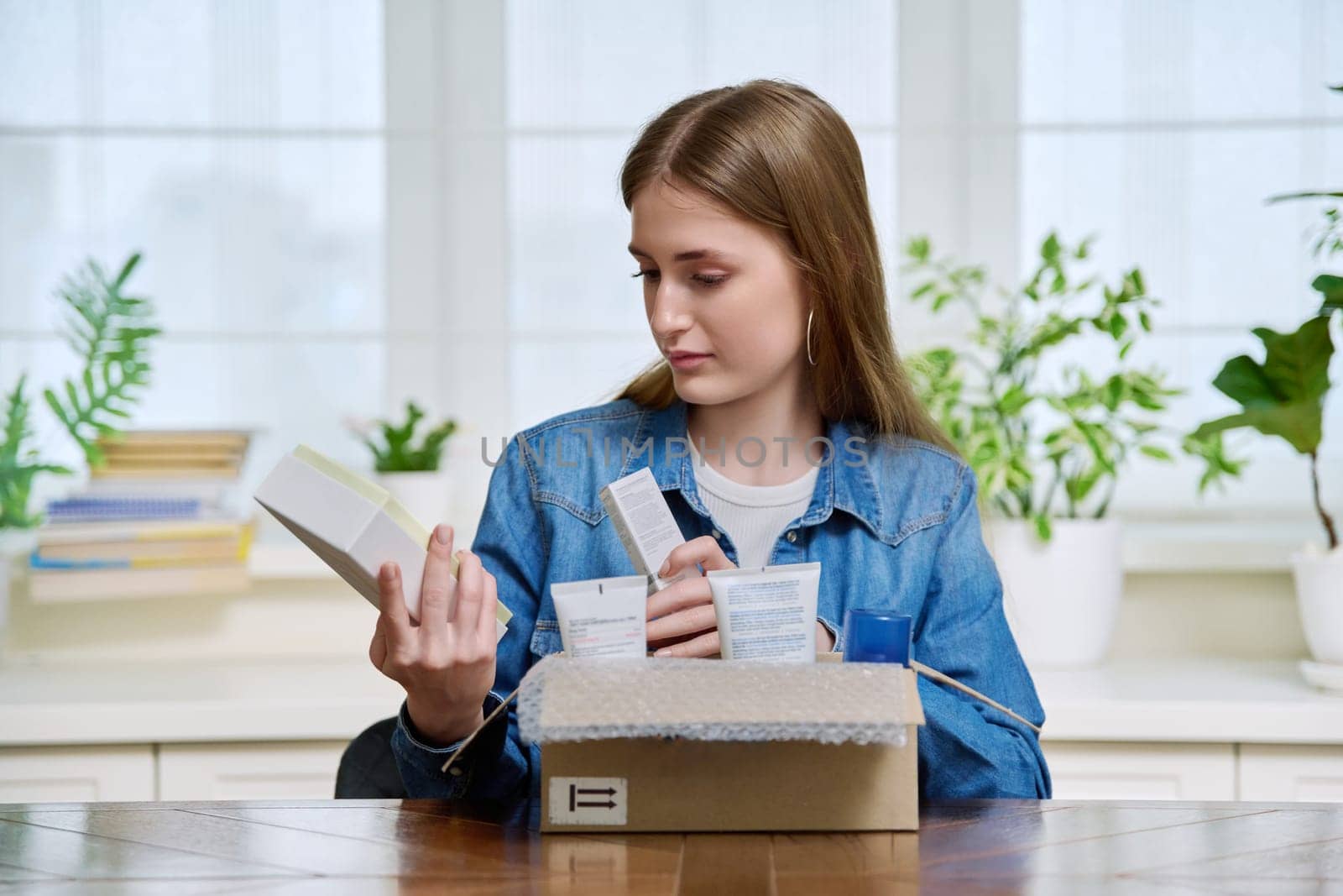 Satisfied young female customer buyer sitting at home unpacking cardboard box with online purchases. Teenage girl unpacking boxes with cosmetics care products perfumes. Delivery by mail, online store