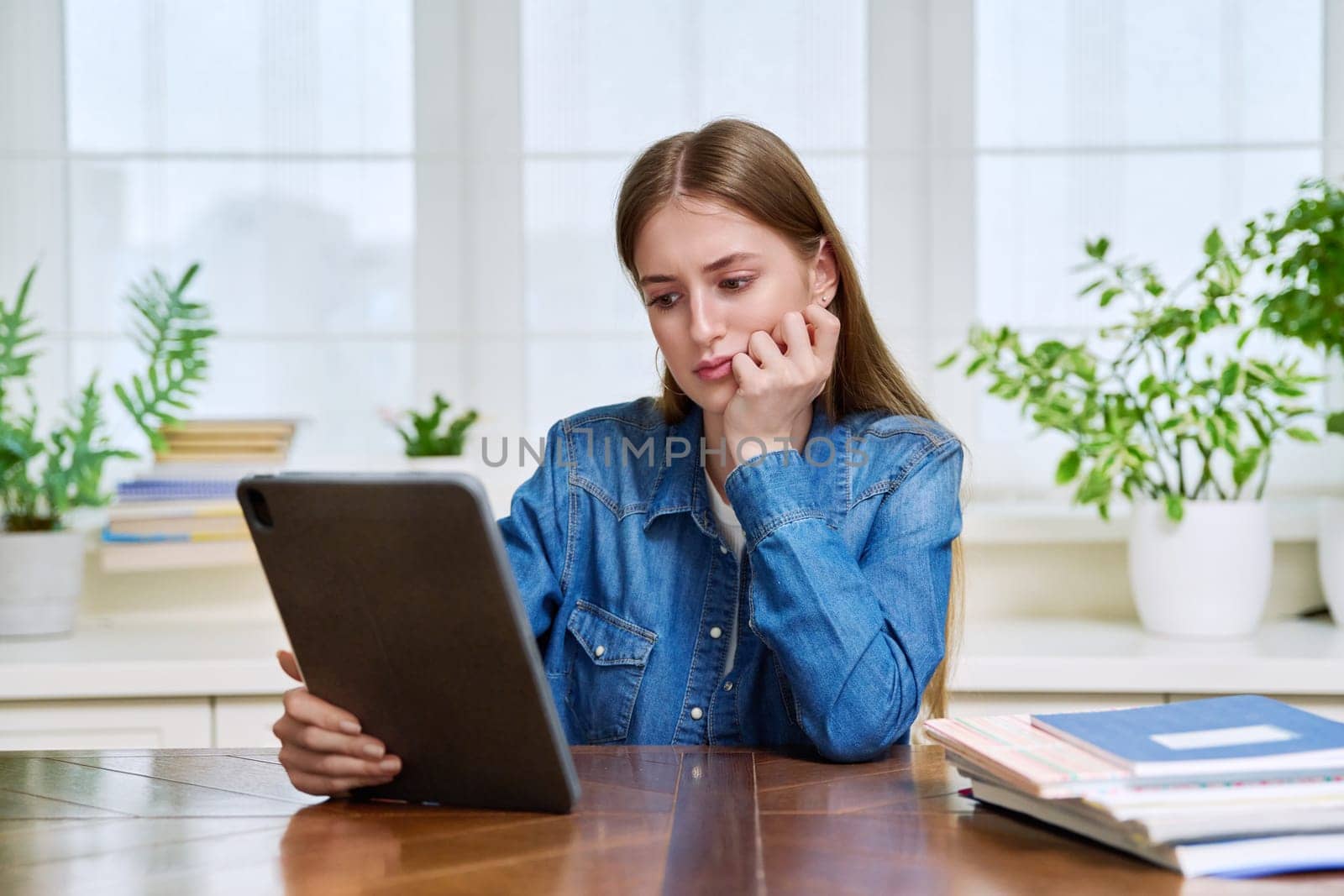 Young teenage female student sitting at home looking talking in web camera of digital tablet. Girl teenager 16,17,18 years old studying remotely, video conference call, e-learning technology education