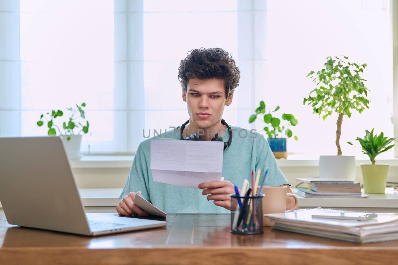 Serious young guy, student of 19-20 years old, reading letter, paper document.