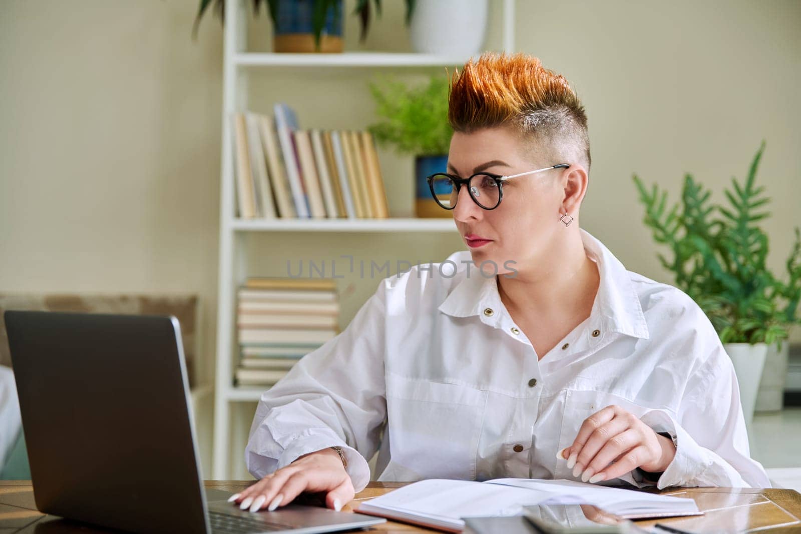 Middle aged woman working with computer papers, remote workplace in home office by VH-studio