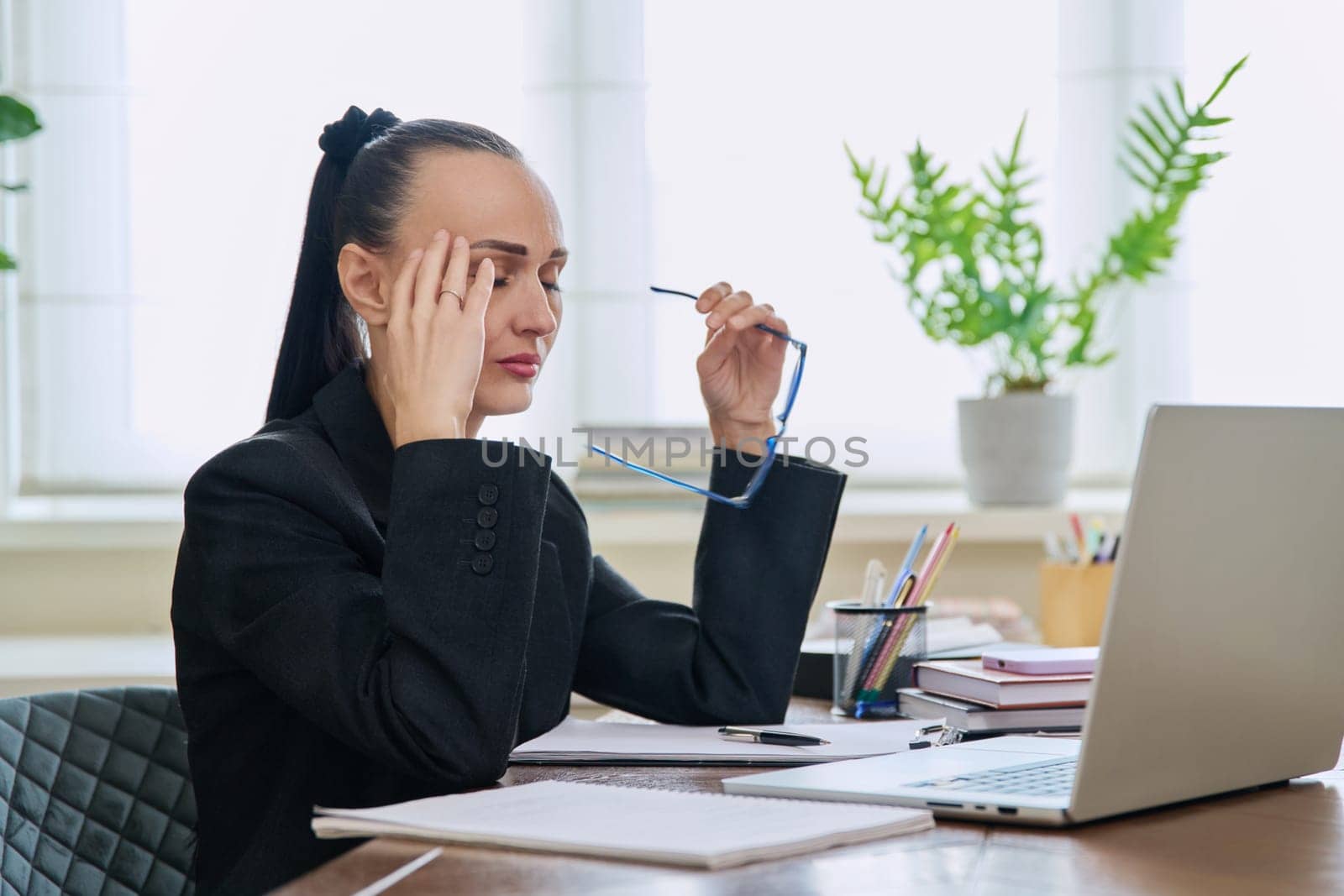 Tired sad business woman at the workplace. Upset female sitting at desk with laptop computer, experiencing stress pain headache. Business, remote work, health problems, freelance concept