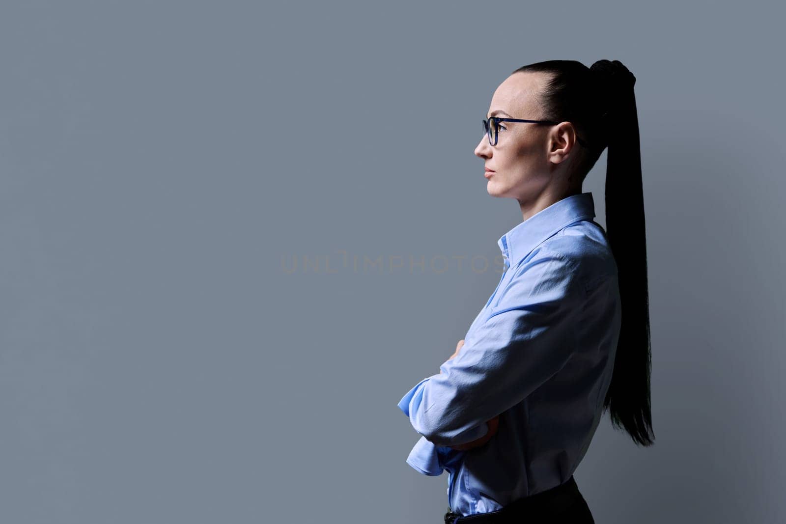 Profile view of middle aged serious woman looking forward, gray studio background, copy space for advertising image text. 30s business confident successful female. Marketing sales services, people