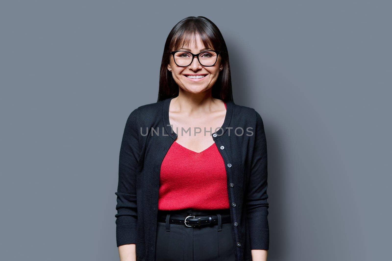 Smiling middle-aged woman on gray studio background. Happy 40s female with glasses looking at camera. Lifestyle, work, beauty, expertise, health, mature people concept