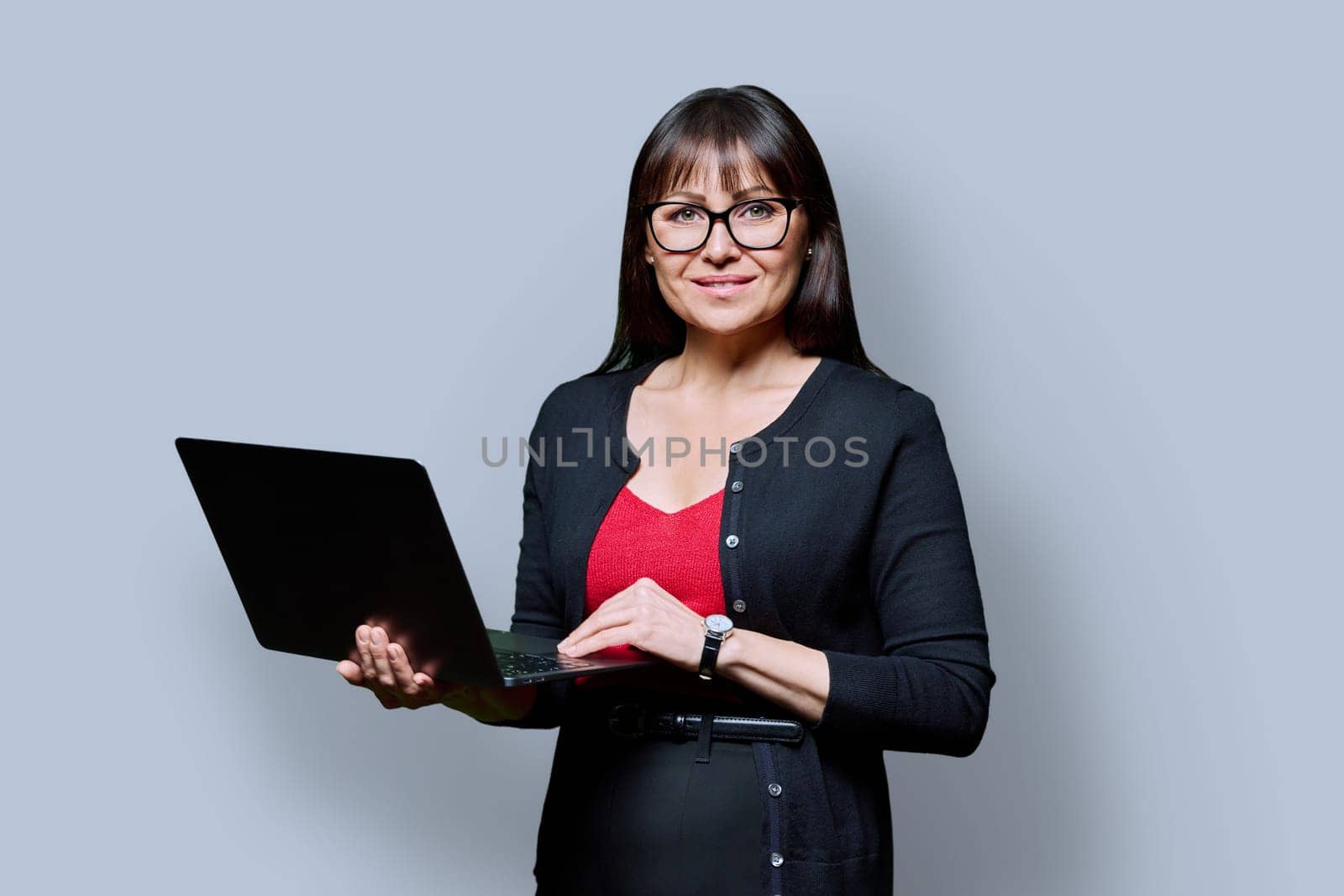 Smiling business middle aged woman using laptop on gray background by VH-studio