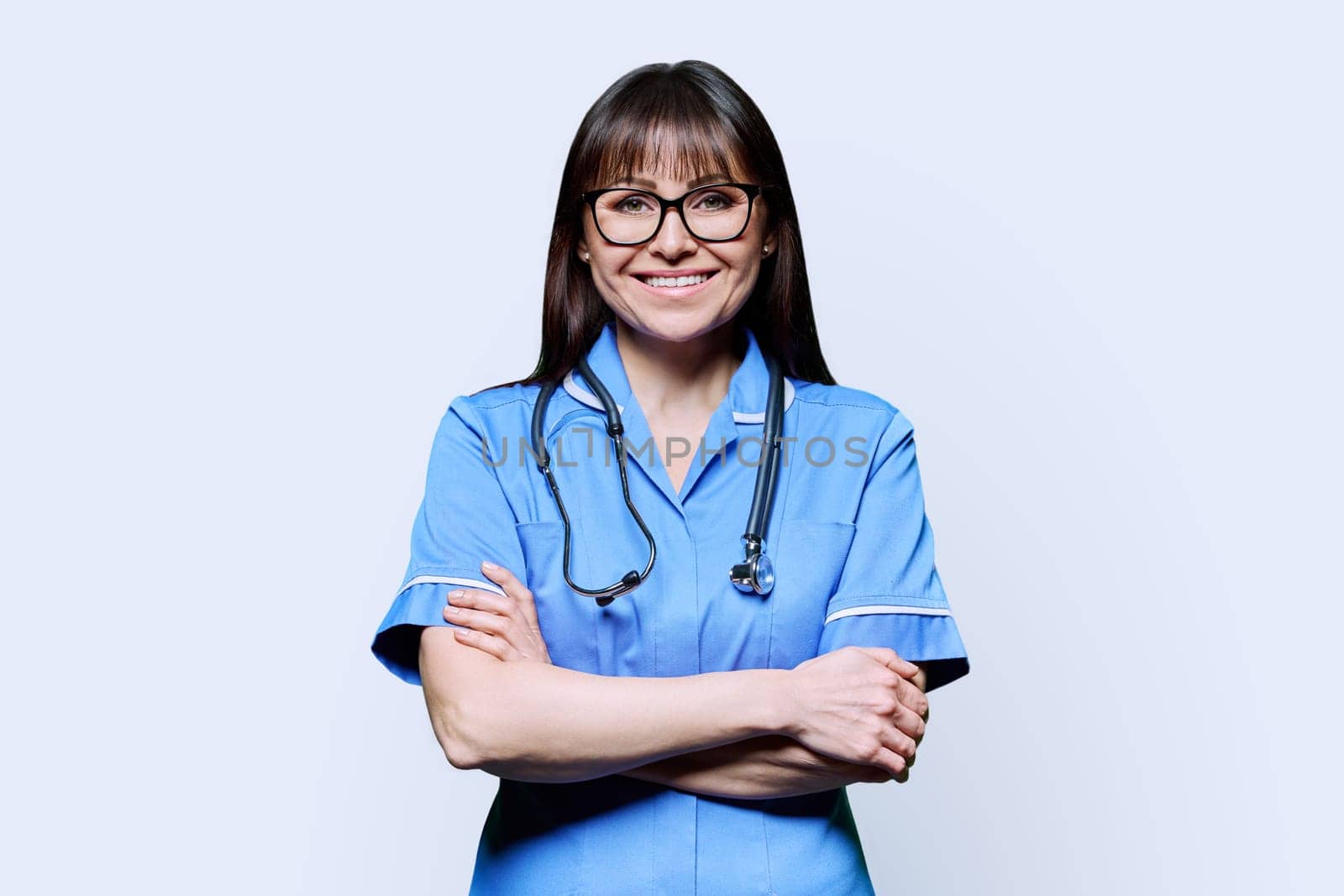Portrait of smiling woman nurse in blue with stethoscope on white background by VH-studio