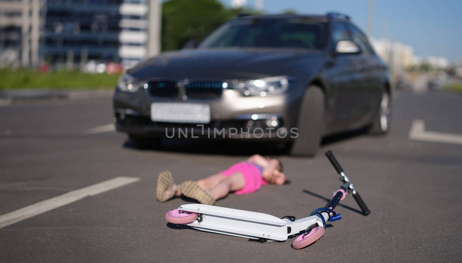 little girl lies on asphalt with scooter after collision with car. Hitting child on the road concept