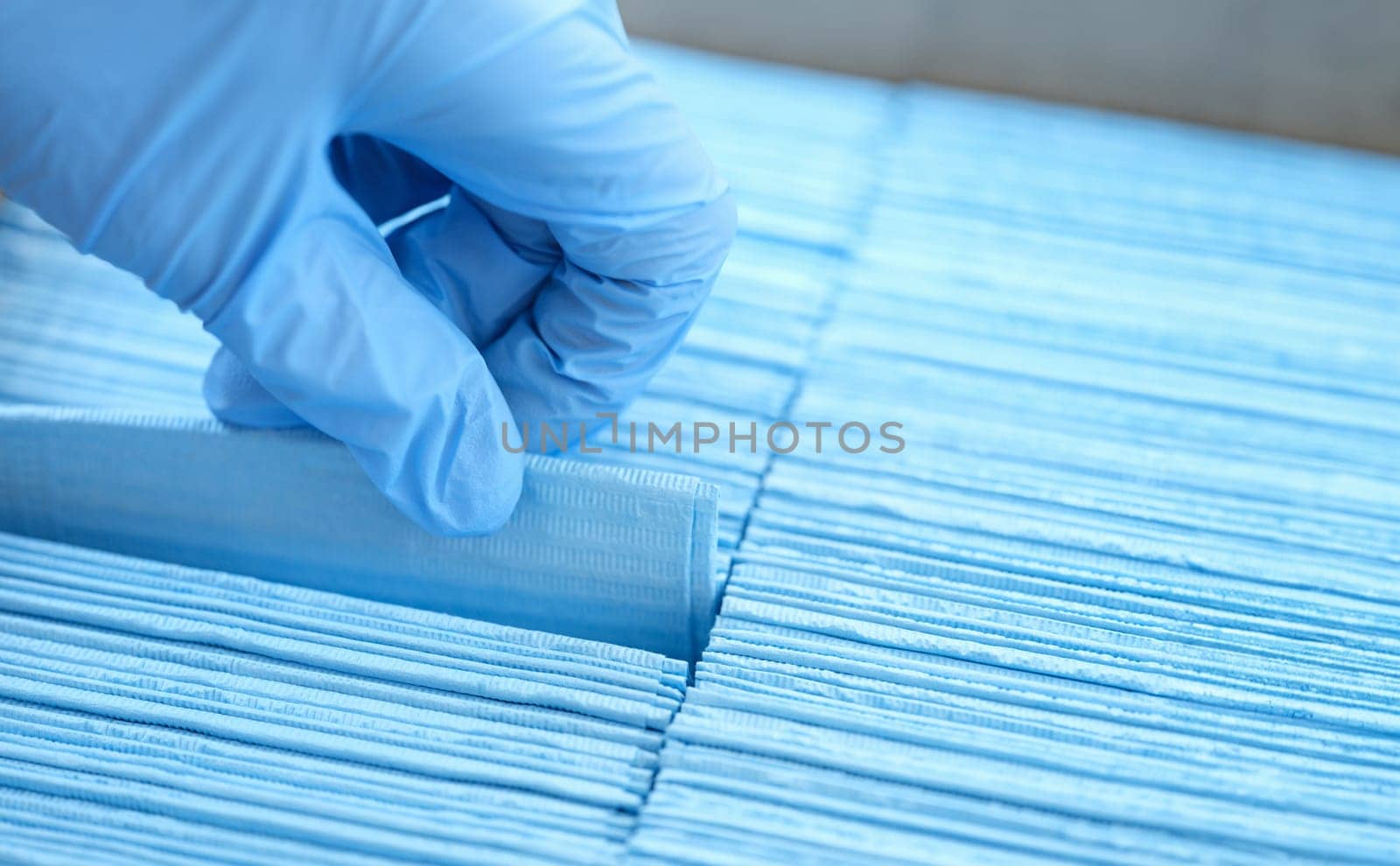 Gloved hand of doctor pulls out disposable blue medical napkin closeup by kuprevich