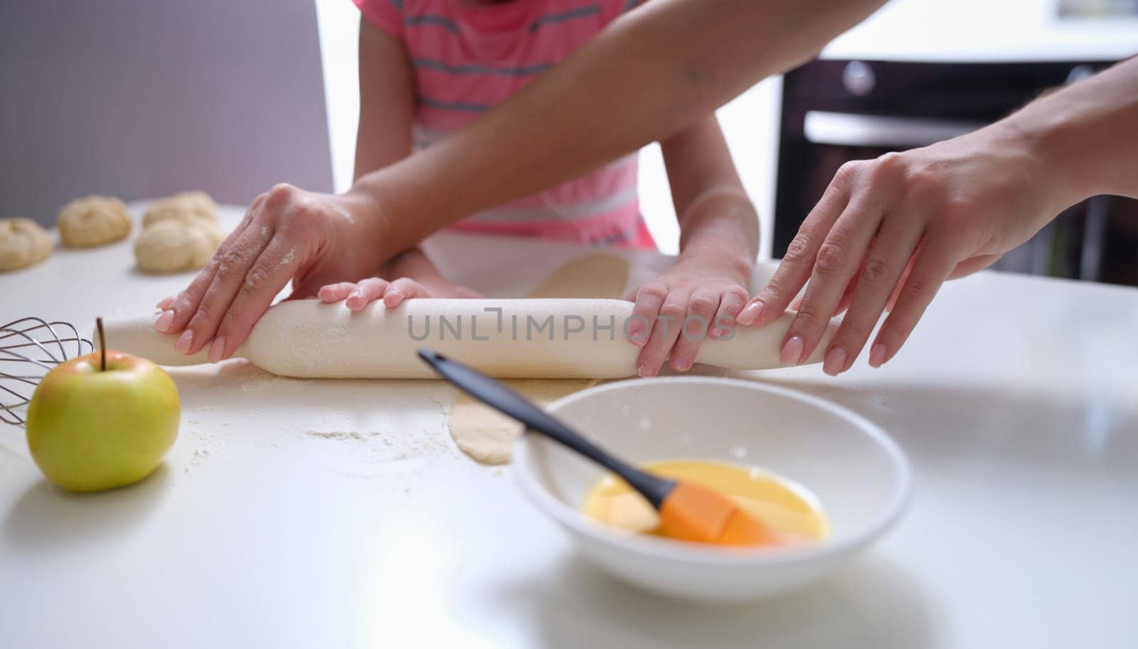 Mother and daughter rolling out flour dough at table closeup by kuprevich