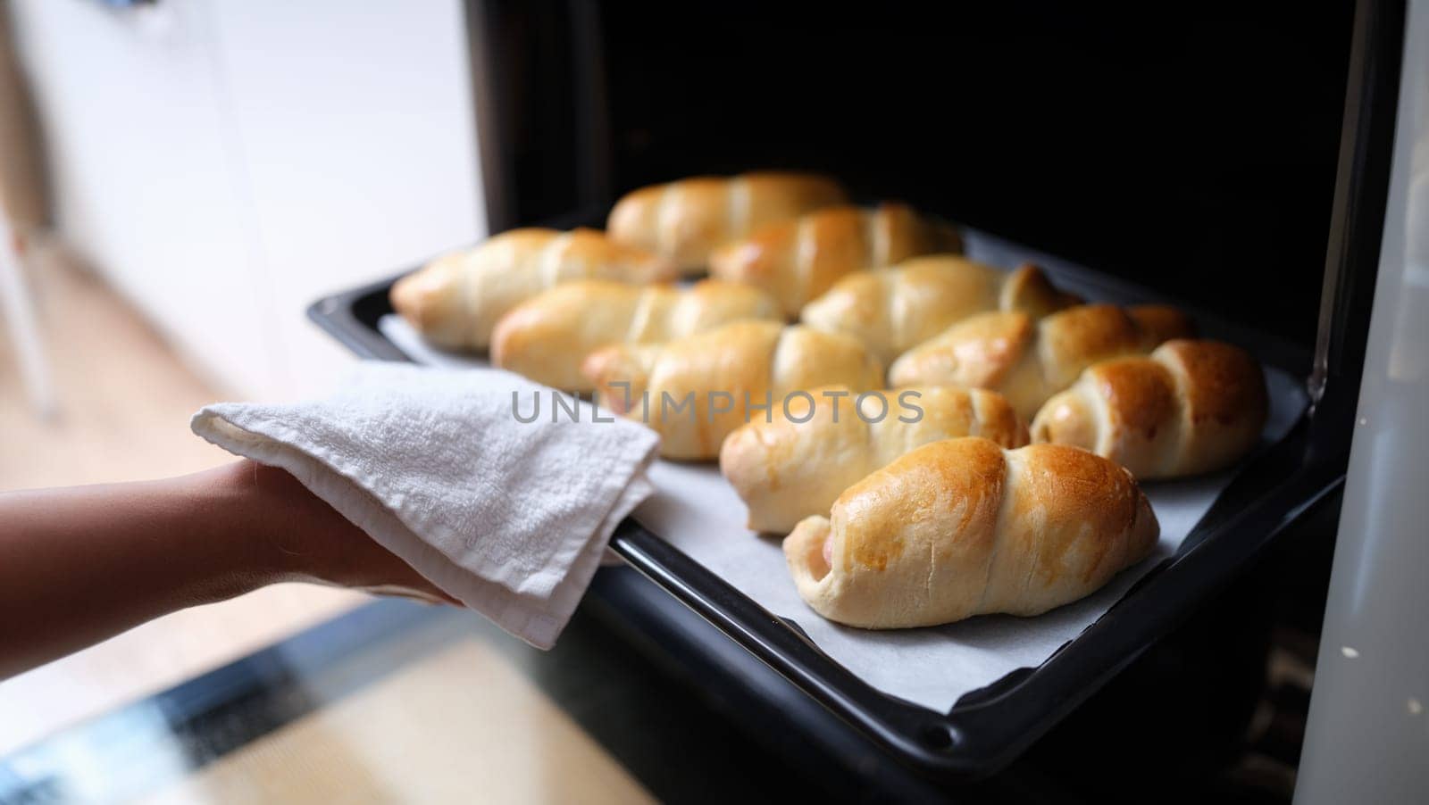 Housewife taking hot delicious mouth watering buns out of oven on baking sheet closeup. Homemade baking concept