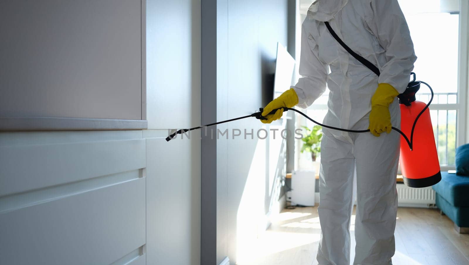 Worker in protective overalls and gloves disinfecting apartment by kuprevich