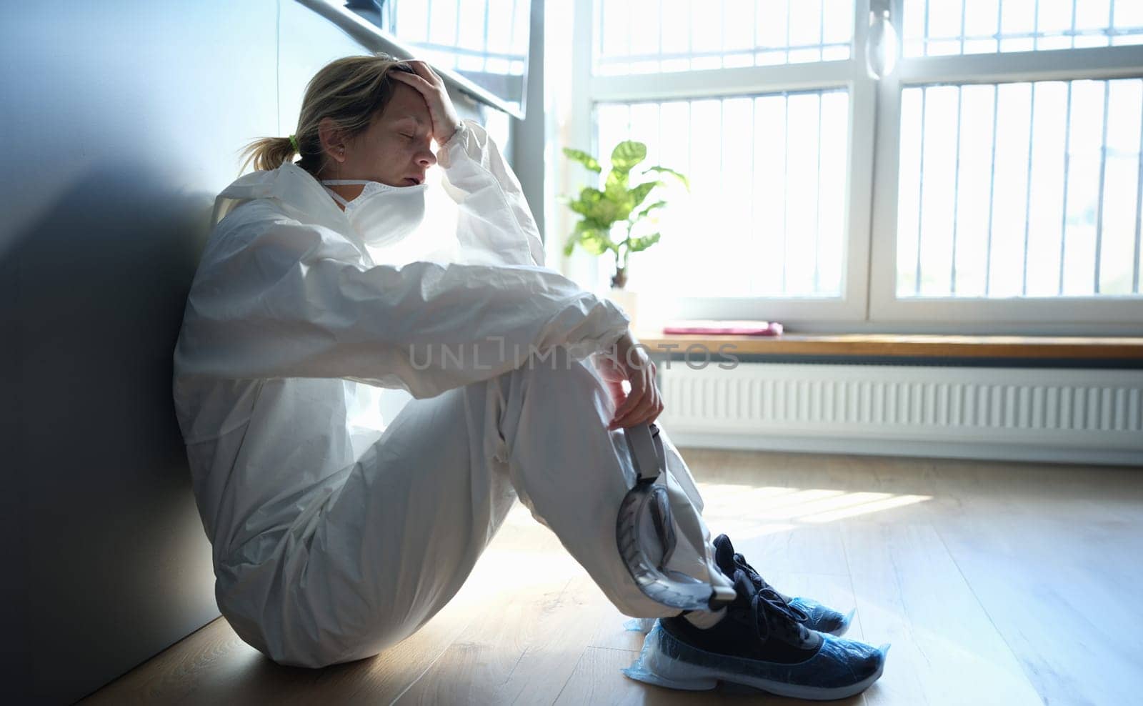 Tired doctor in protective antiplague suit sitting on corridor of clinic by kuprevich