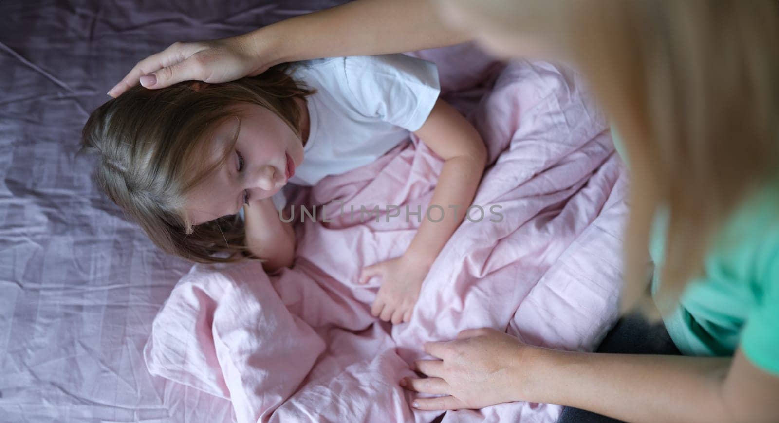 Mother stroking head of little sad girl lying in bed. Psychological problems in children concept