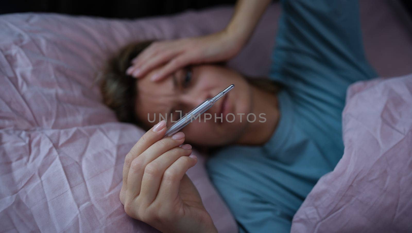 Sick woman lying in bed and holding thermometer with high temperature closeup. Seasonal colds home treatment concept