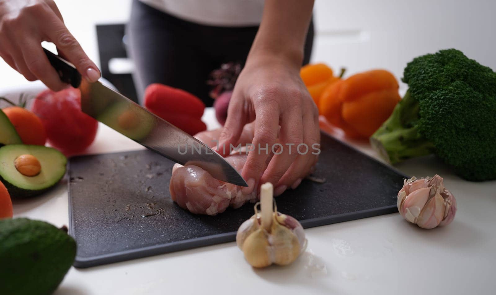 Chef cutting meat on board near vegetables closeup. Healthy nutritious food concept