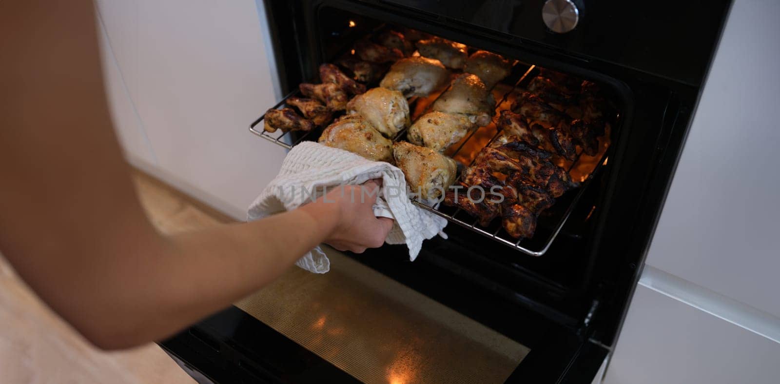 Woman taking out grill of baked chicken from oven closeup. Recipes for cooking in oven concept