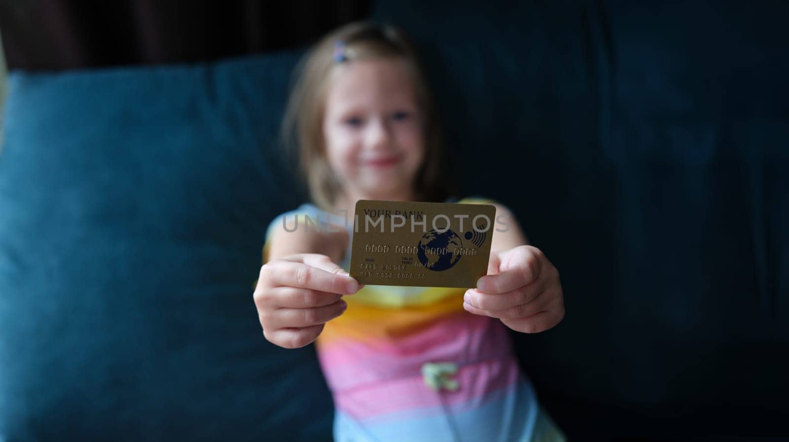 Little girl holding plastic credit bank card at home closeup. Paid children education concept