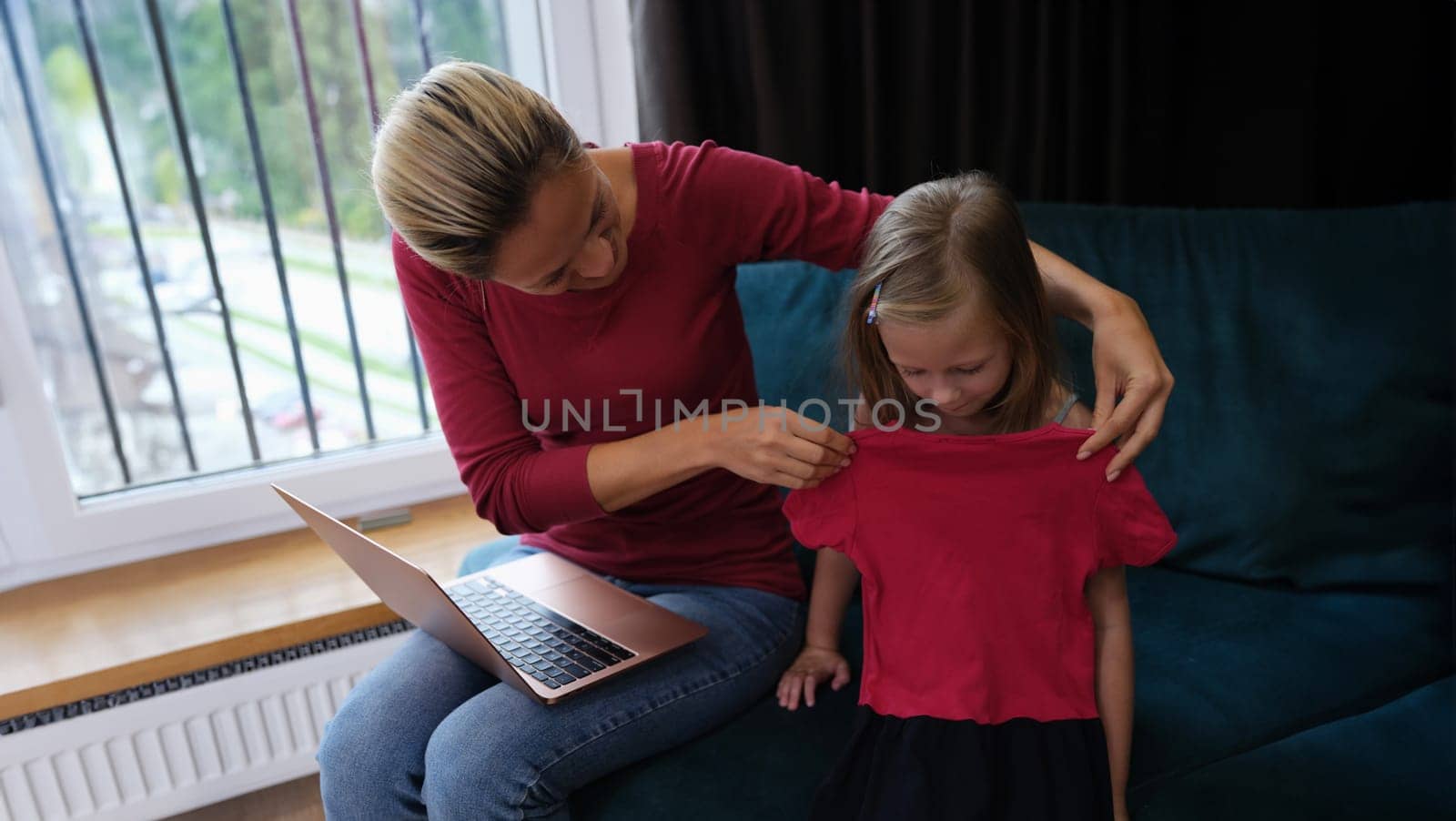 Mom and daughter are sitting on couch with laptop and trying on dress. Online shopping concept