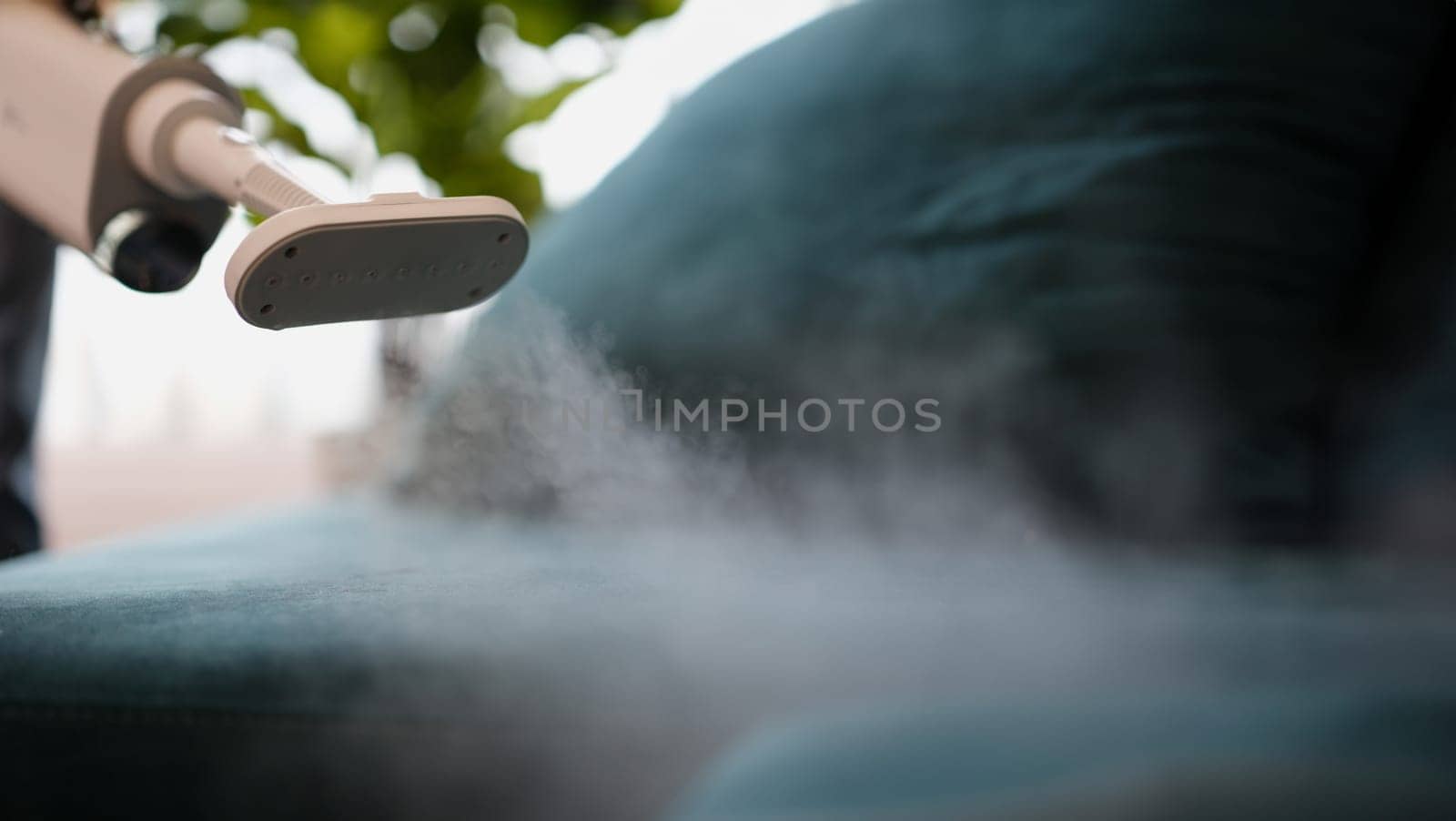 Cleaner washing green sofa with steamer at home closeup by kuprevich