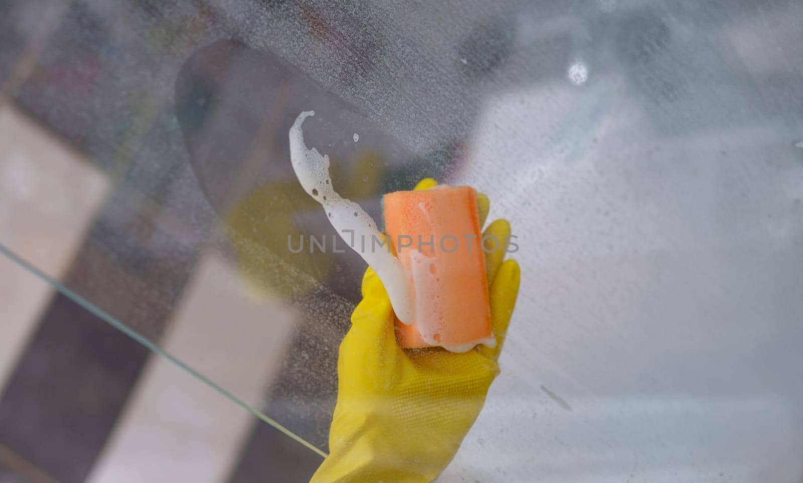 Cleaner in rubber gloves washing glass in bathroom with detergent and sponge closeup by kuprevich