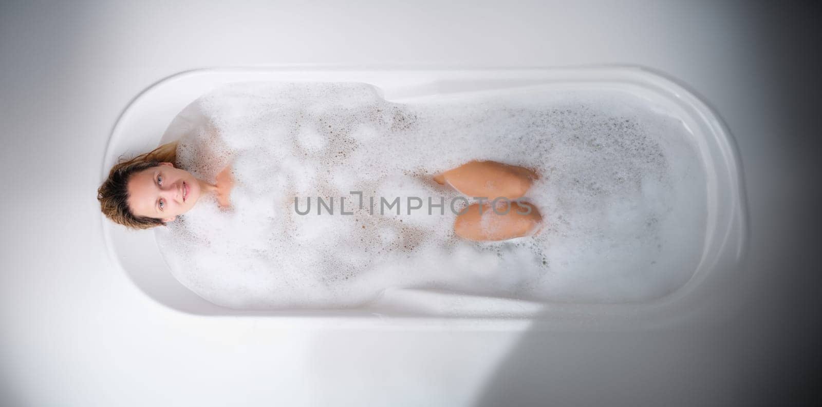 Young woman lying in warm bath with foam top view. Body care concept