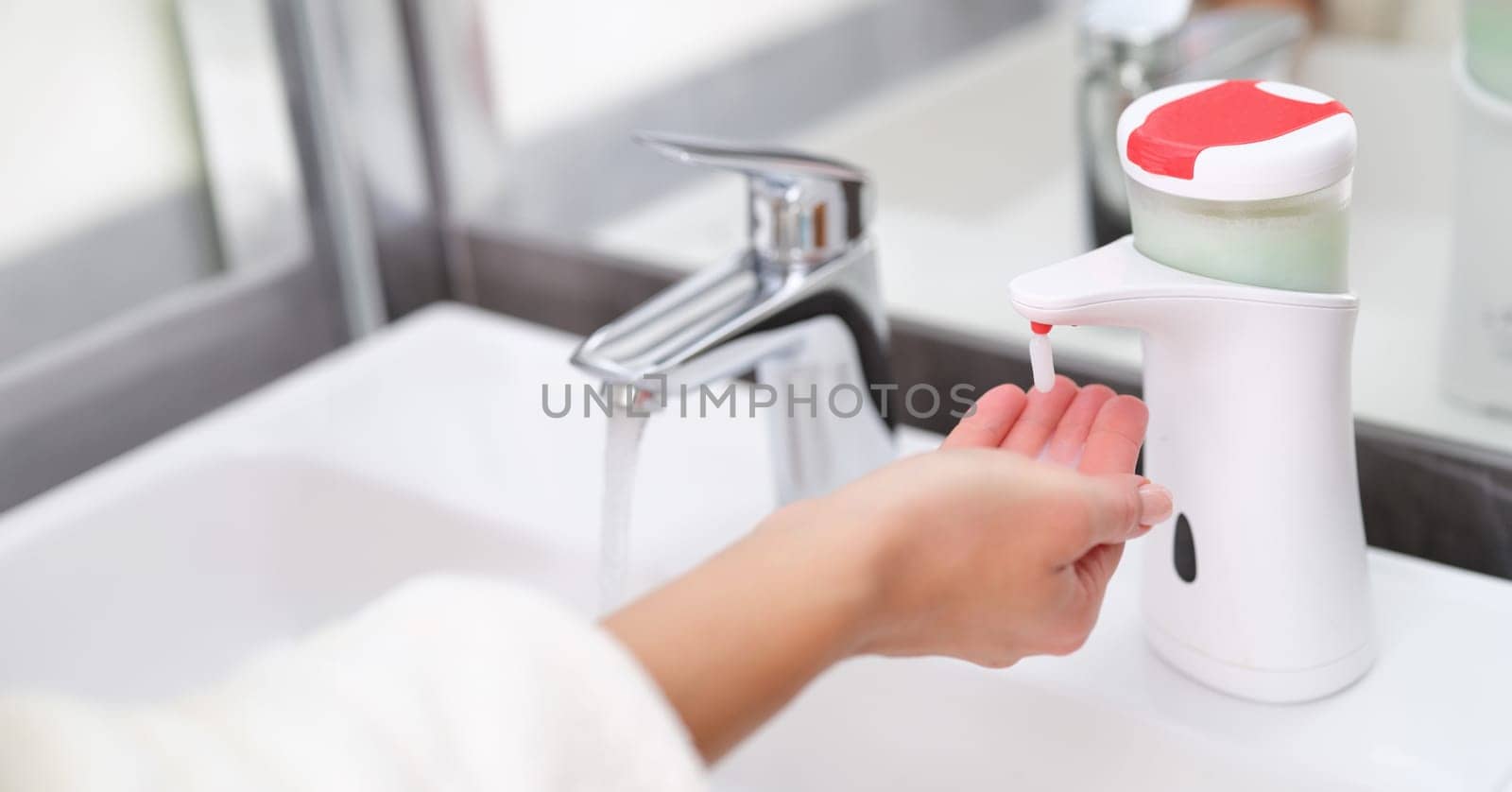 Woman picking up liquid soap from hand dispenser in bathroom closeup by kuprevich