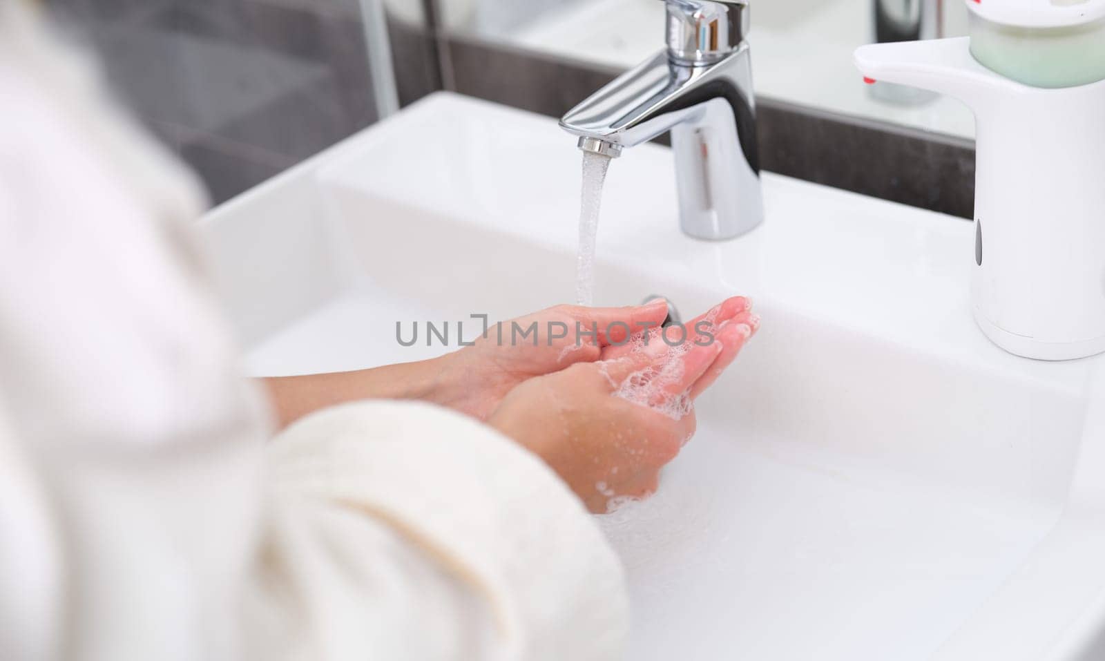 Woman washing her hands under water from tap in bathroom closeup. Hand hygiene concept