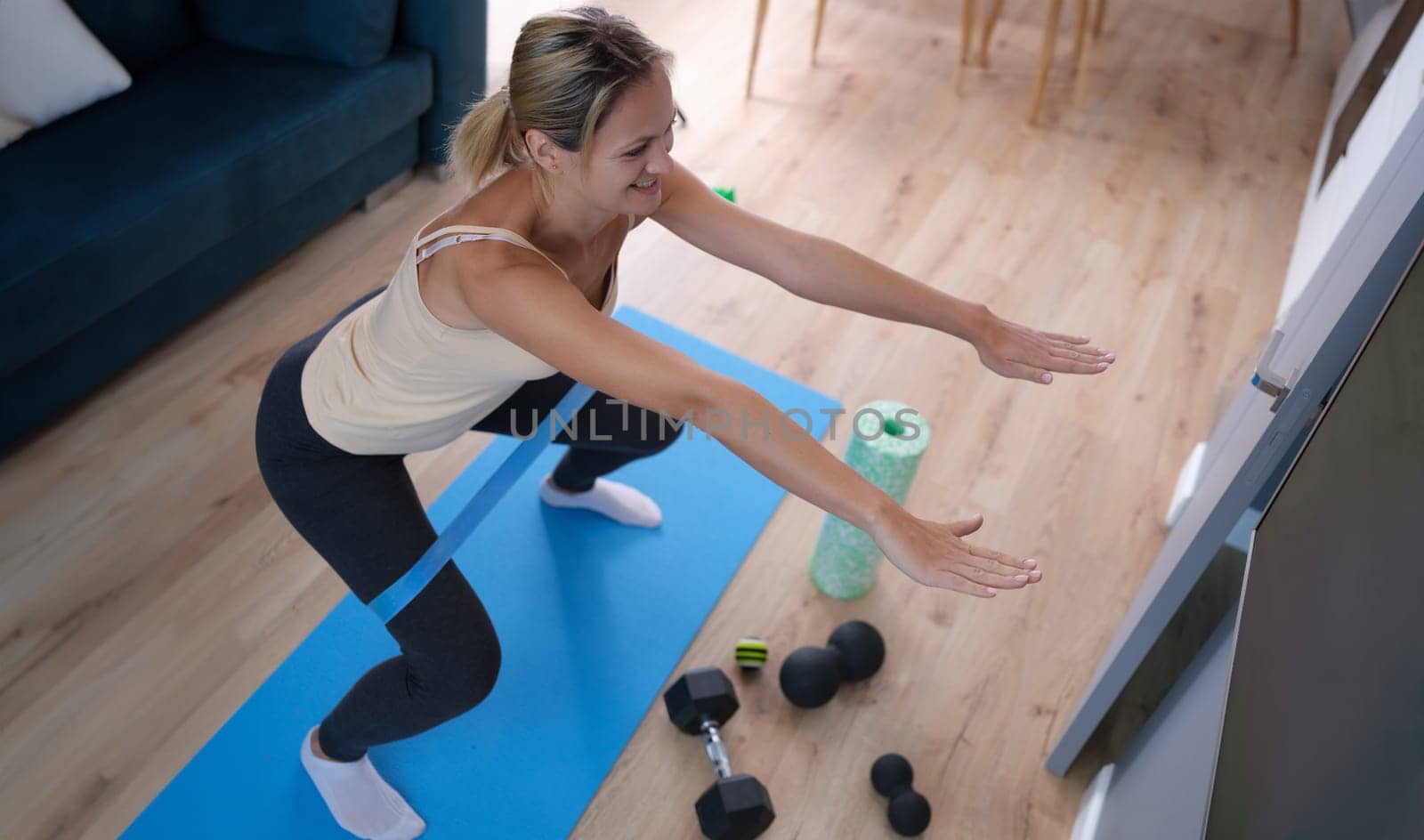 Young woman squatting with elastic band on her legs at home. Remote fitness concept